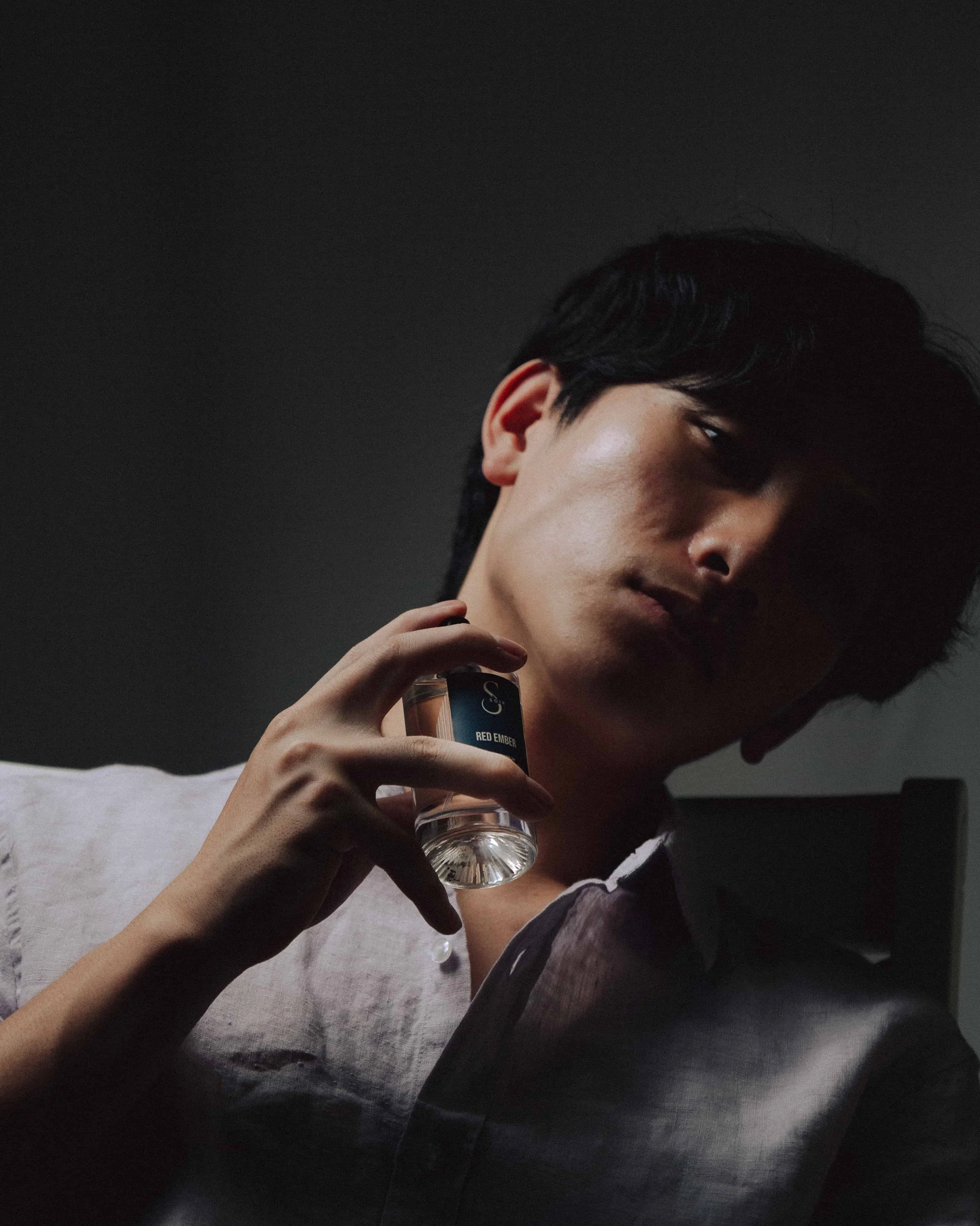 man holding bottle of fragrance around his neck with a dramatic shadow