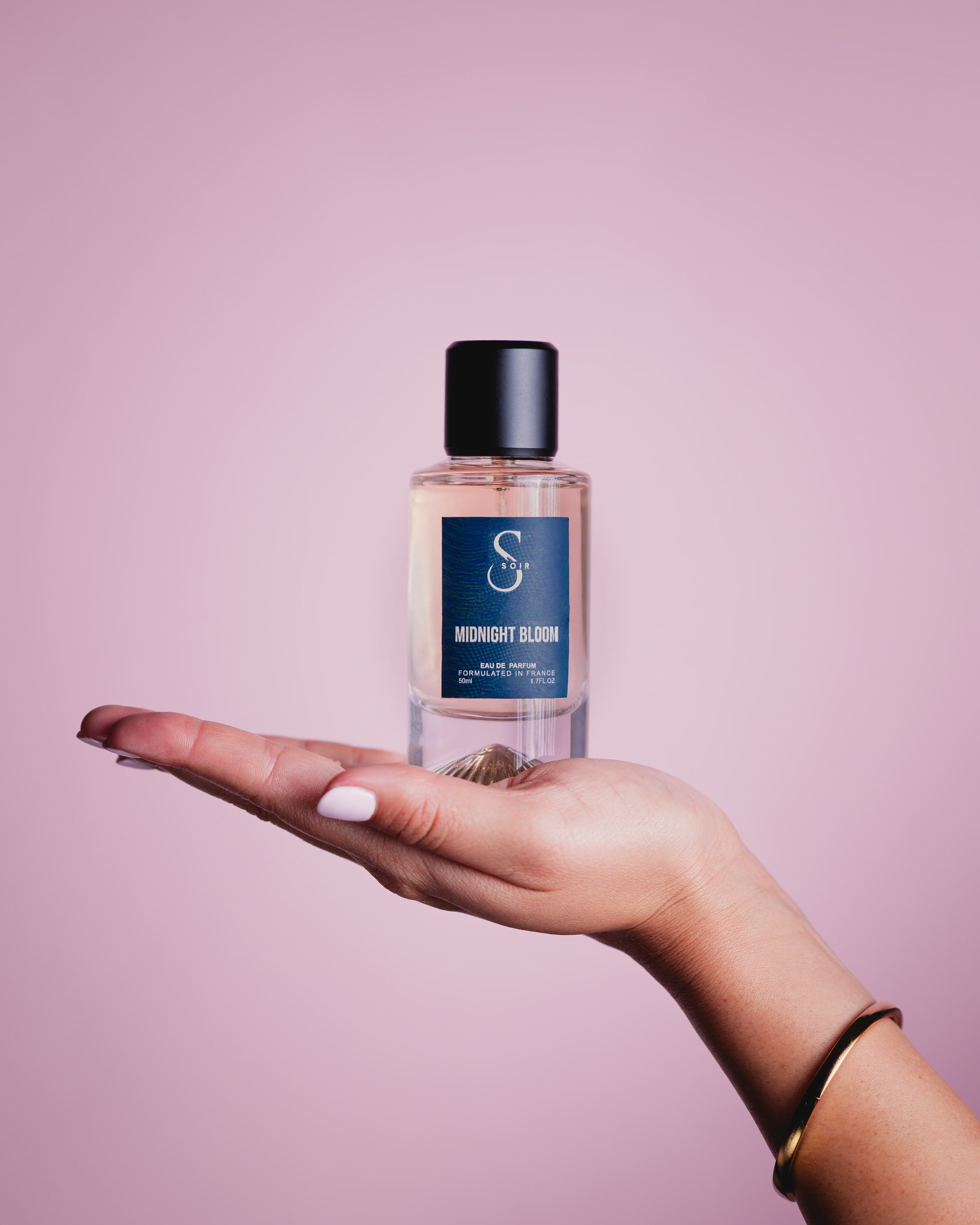 woman's hand with a bottle of perfum on her palm witha. pink background
