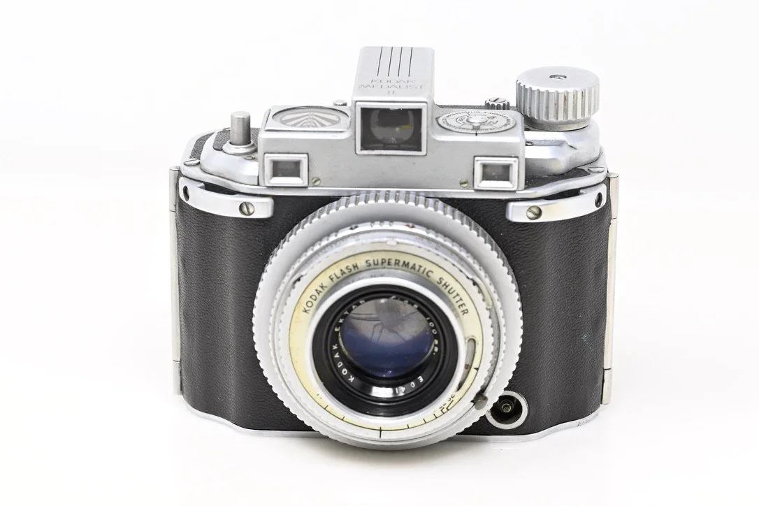 Vintage camera with black leather and silver metal accents, featuring a Kodak flash supermatic shutter lens, set against a plain white background.
