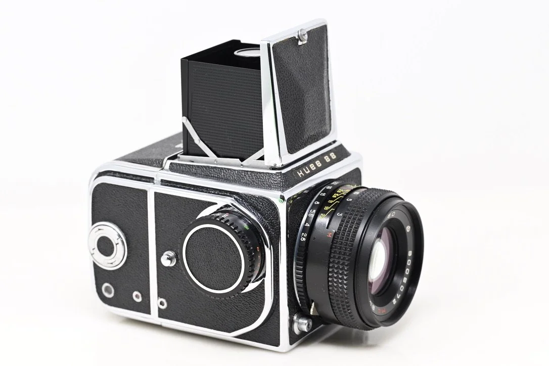 Black vintage film camera with a large lens and a flat, open viewfinder on top.