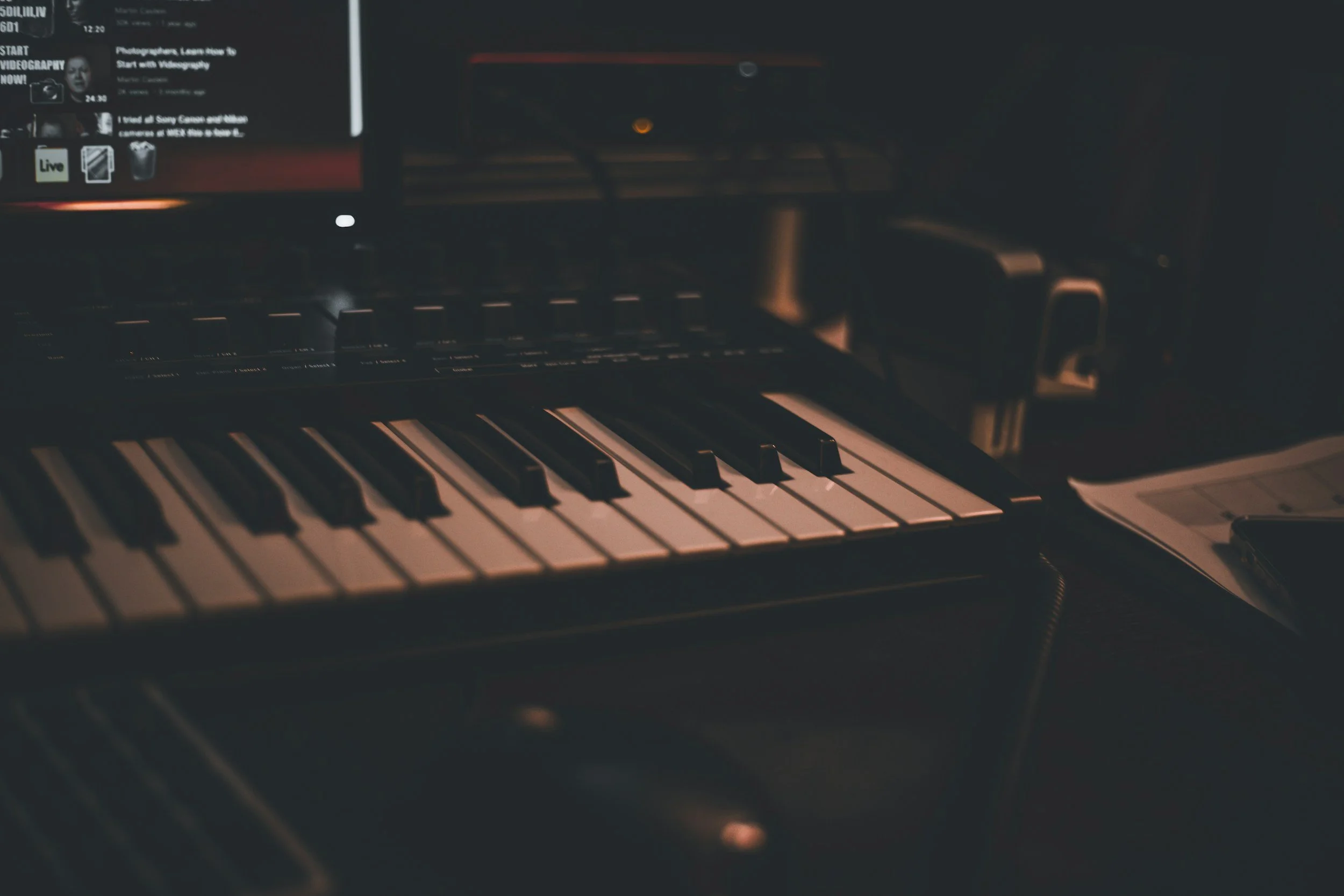Close-up of a digital music keyboard on a dark desk with a computer screen in the background.
