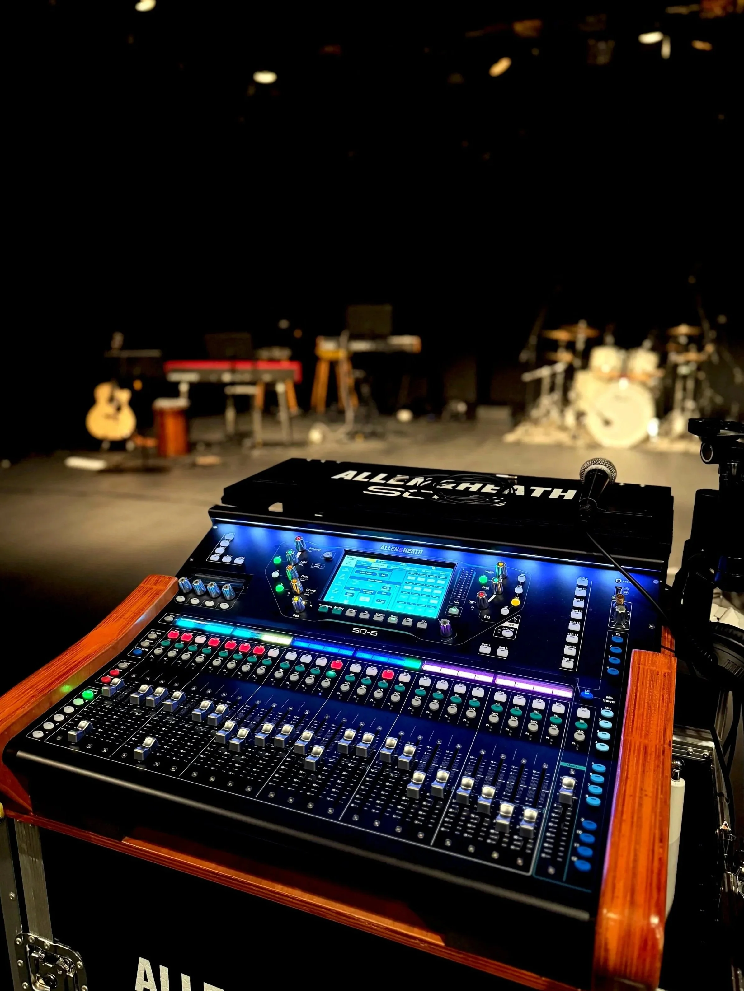 A stage with musical instruments and equipment, including a drum set, guitars, and keyboards, with a sound mixing console in the foreground.