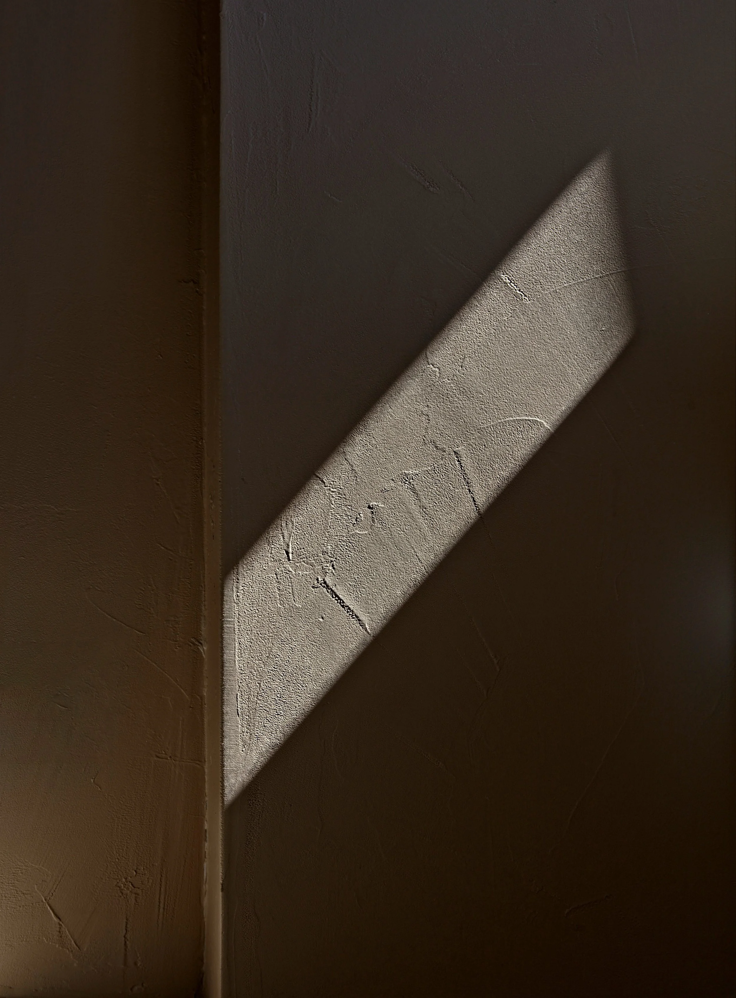 Sunlight creating a shadow on a textured wall.