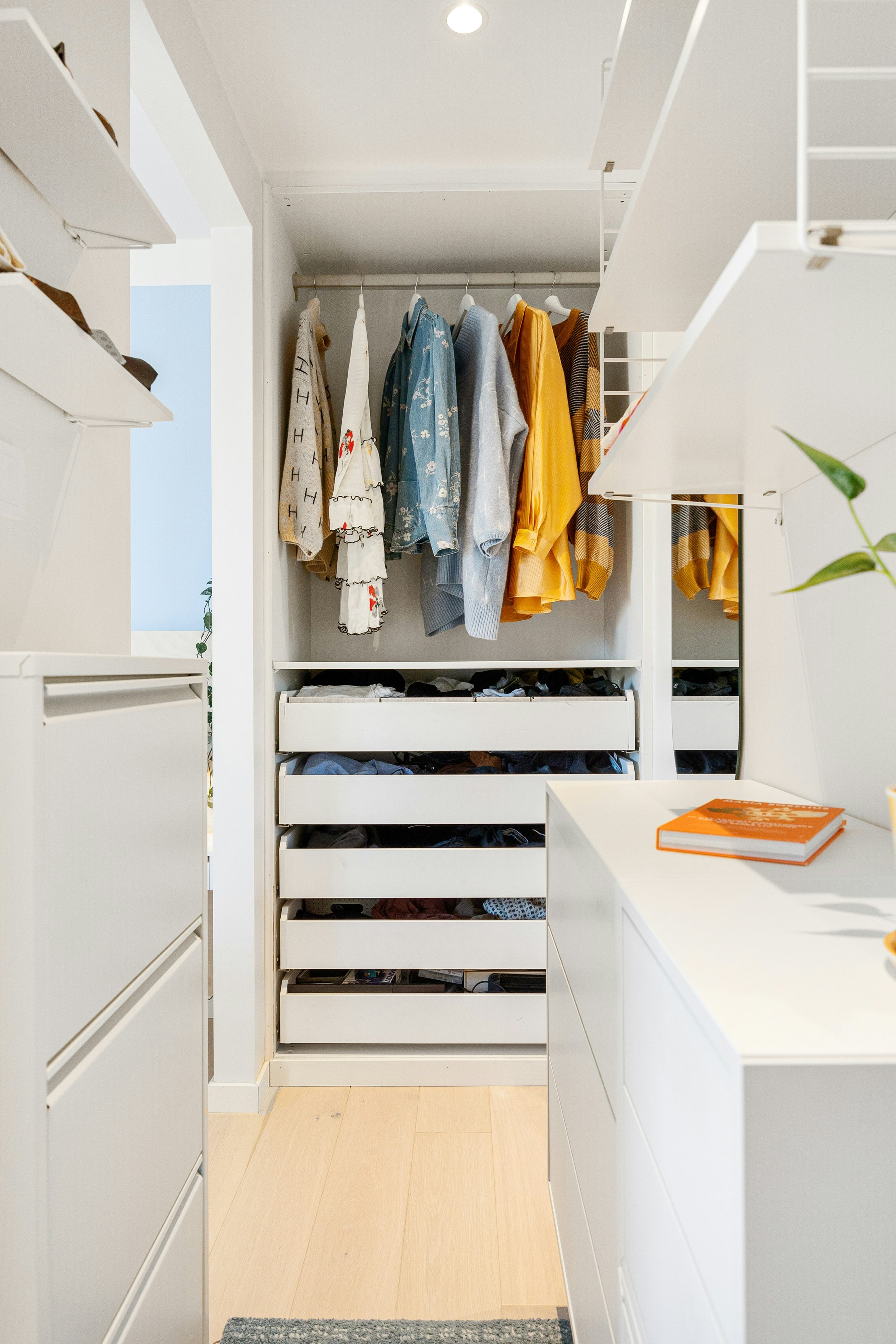 Closet with hanging clothes and drawers filled with shoes.