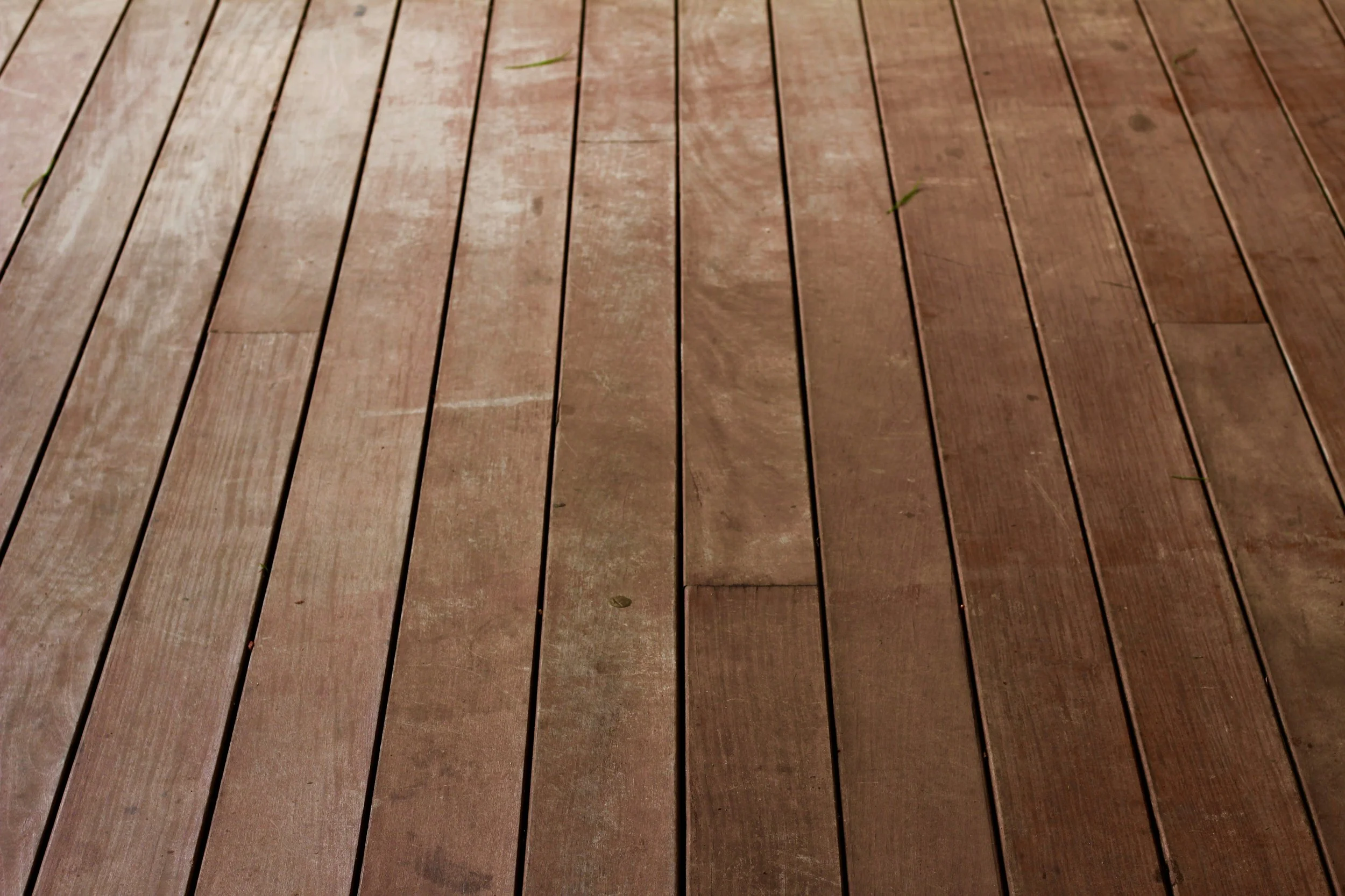 Wooden deck with evenly spaced planks and a few small leaves scattered on the surface.