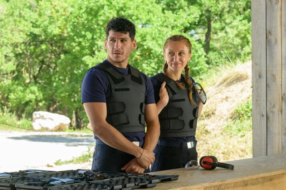 Deux policiers en gilet pare-balles se tiennent à côté d'une table avec des outils, dans un environnement extérieur vert.