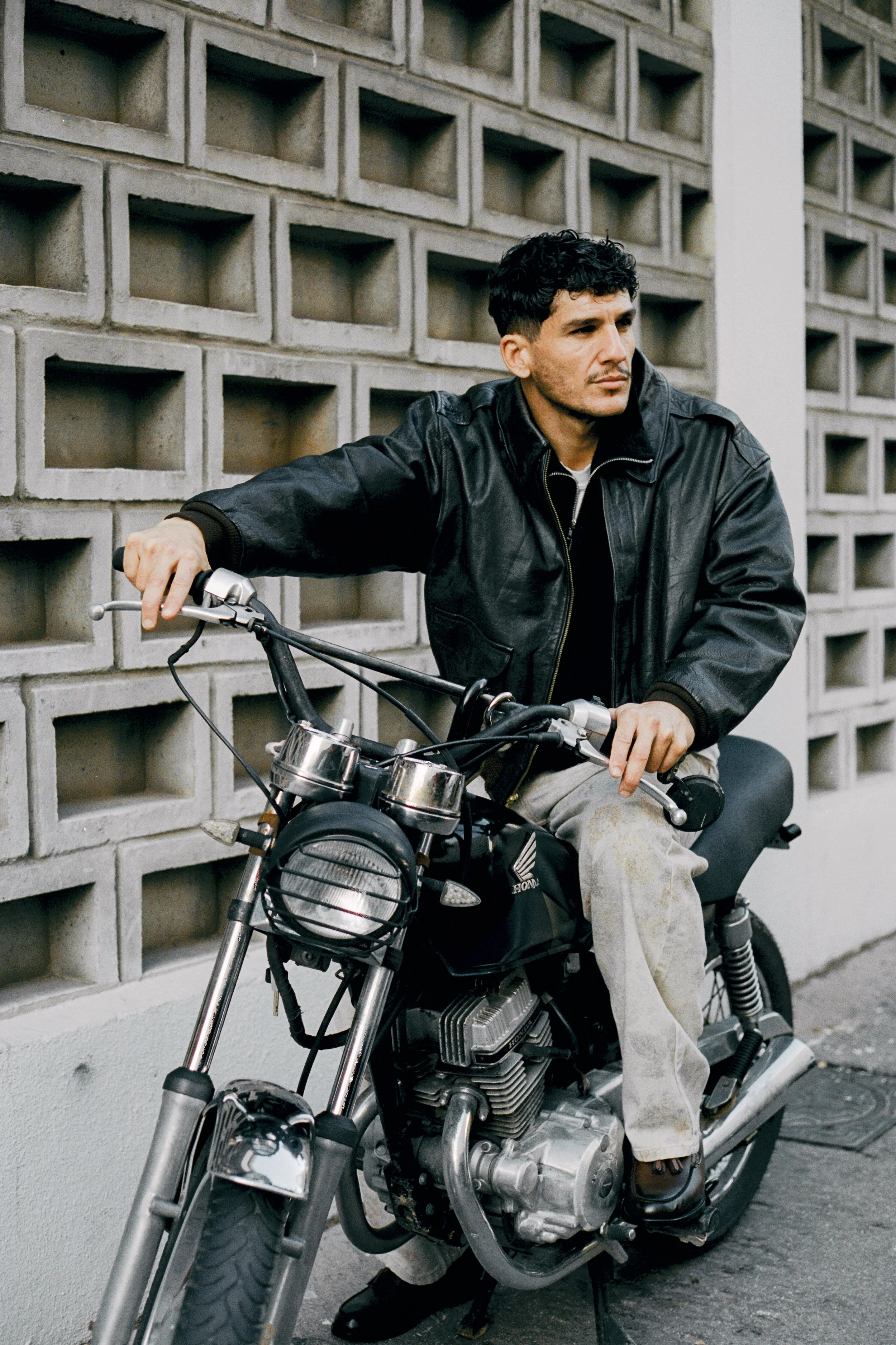 Un homme en veste en cuir assis sur une moto à côté d'un mur en béton.