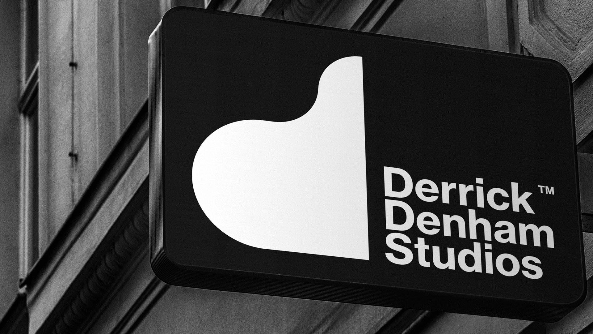 Signboard for Derrick Denham Studios with a stylized 'D' logo on a building's exterior wall in black and white.