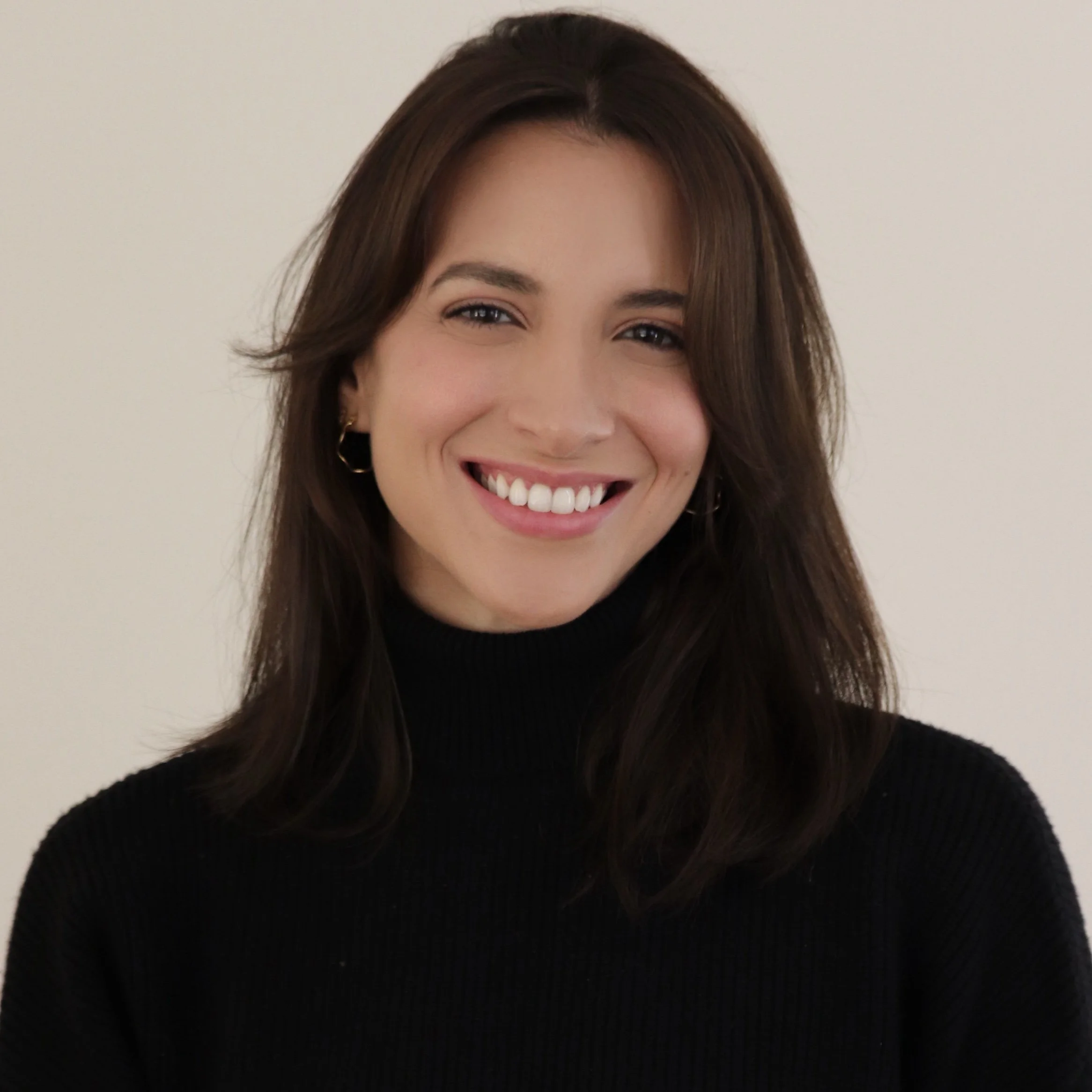 A woman with dark brown hair, wearing a black turtleneck sweater, smiling with white teeth