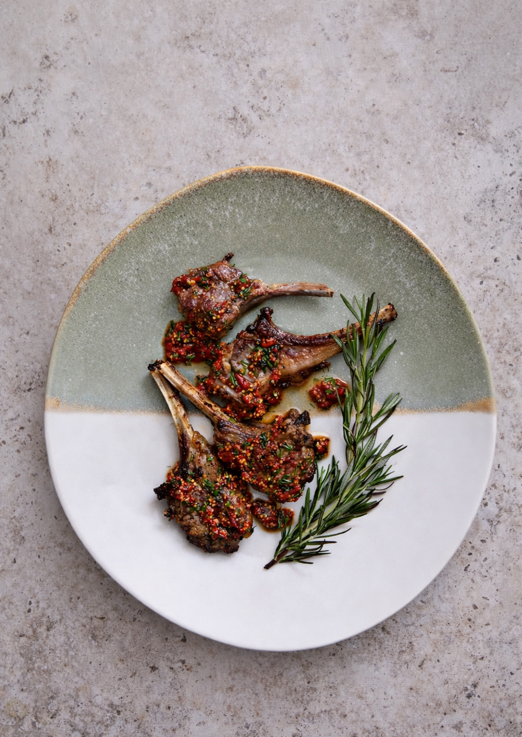 Plate with grilled lamb chops topped with a spicy red sauce and garnished with fresh rosemary.