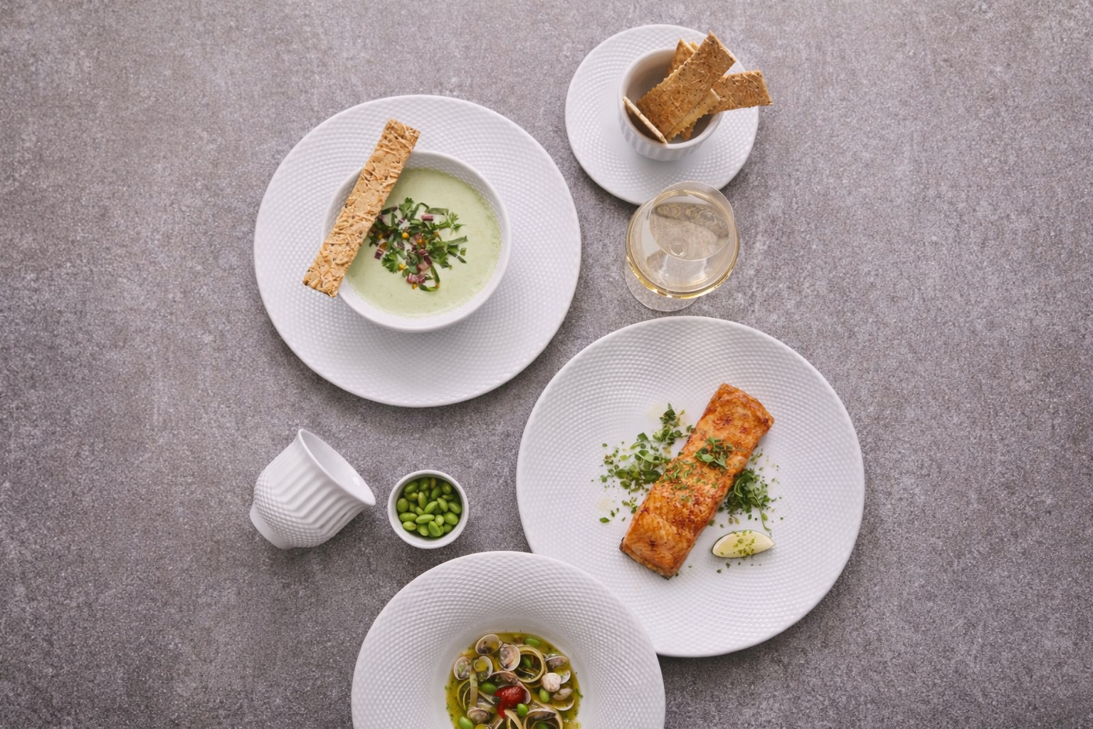 Top-down view of an elegant meal with seafood, soup, bread, and drinks on textured gray table.