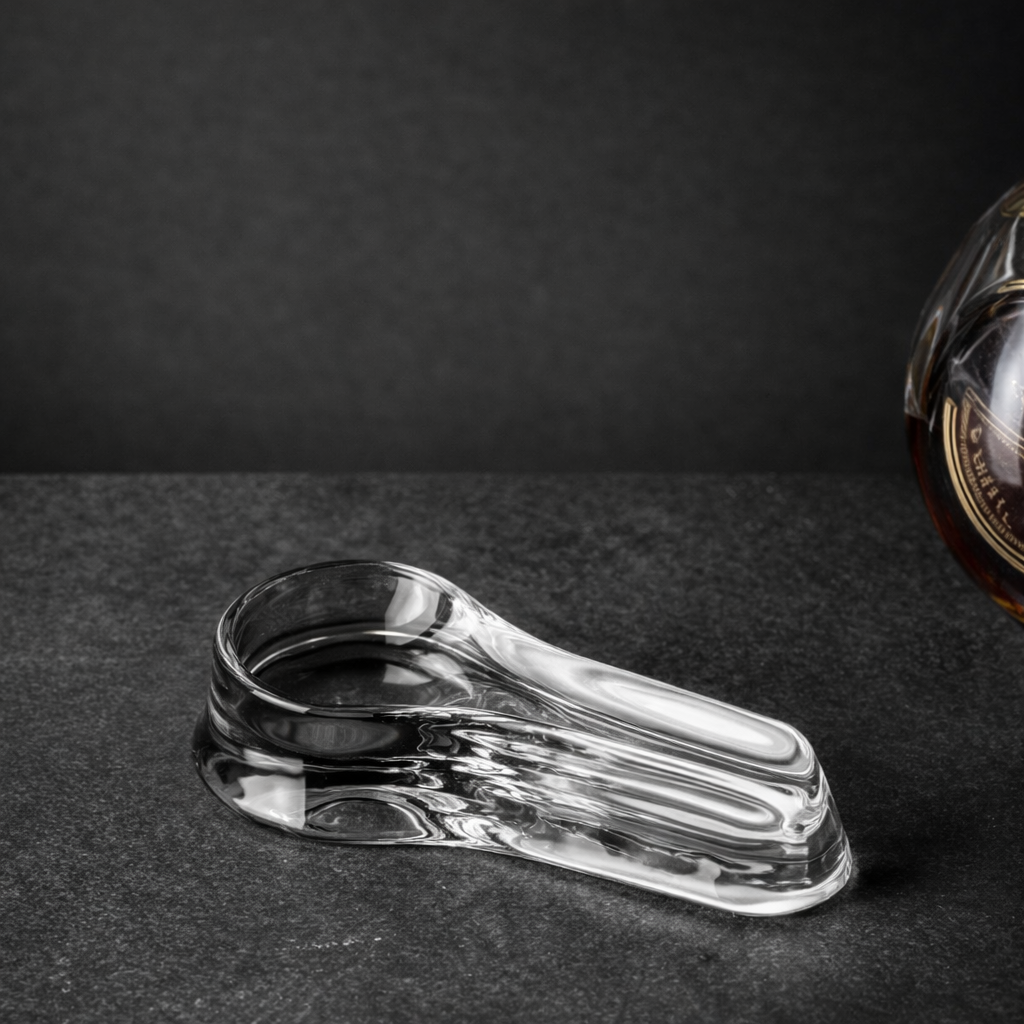 A clear glass whiskey decanter with a round stopper and a matching glass ashtray. The decanter is partially visible on the right side.