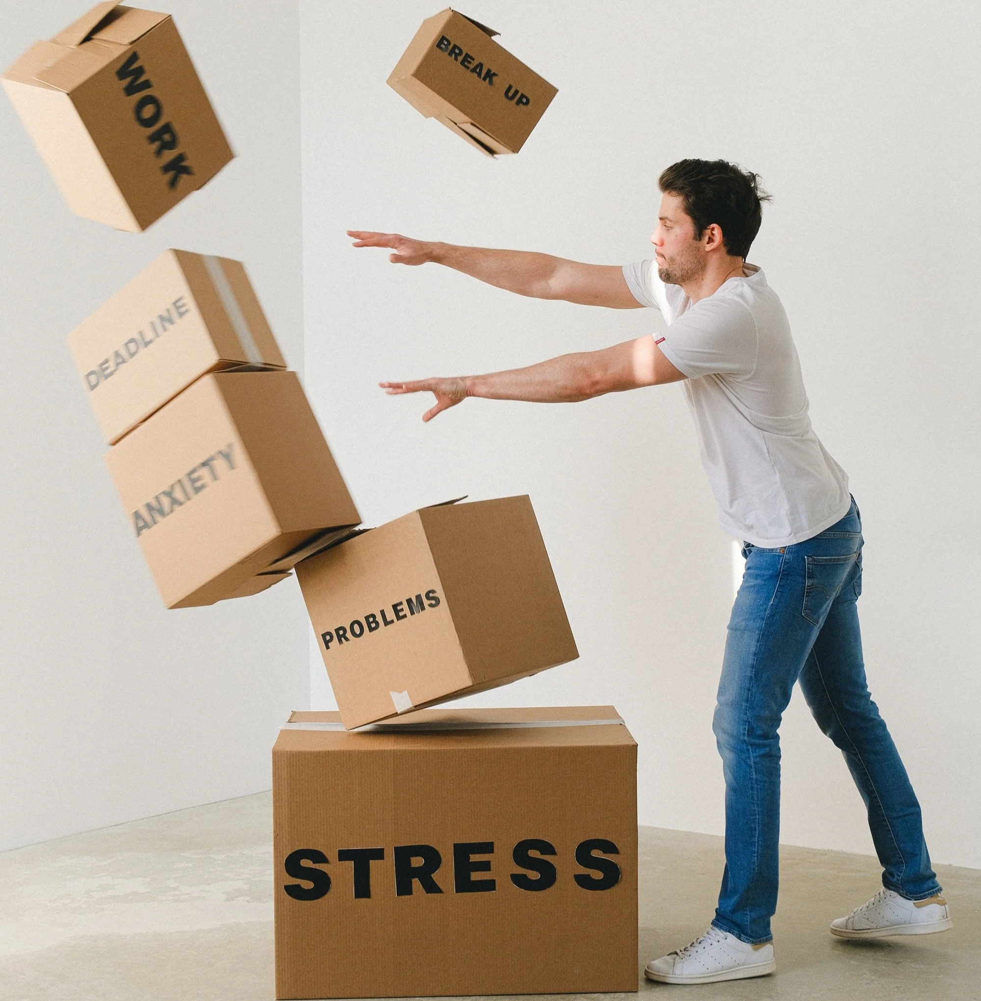 A man throws cardboard boxes labeled with words like 'Work,' 'Deadline,' 'Anxiety,' 'Problems,' and 'Break Up' into a box labeled 'Stress.'