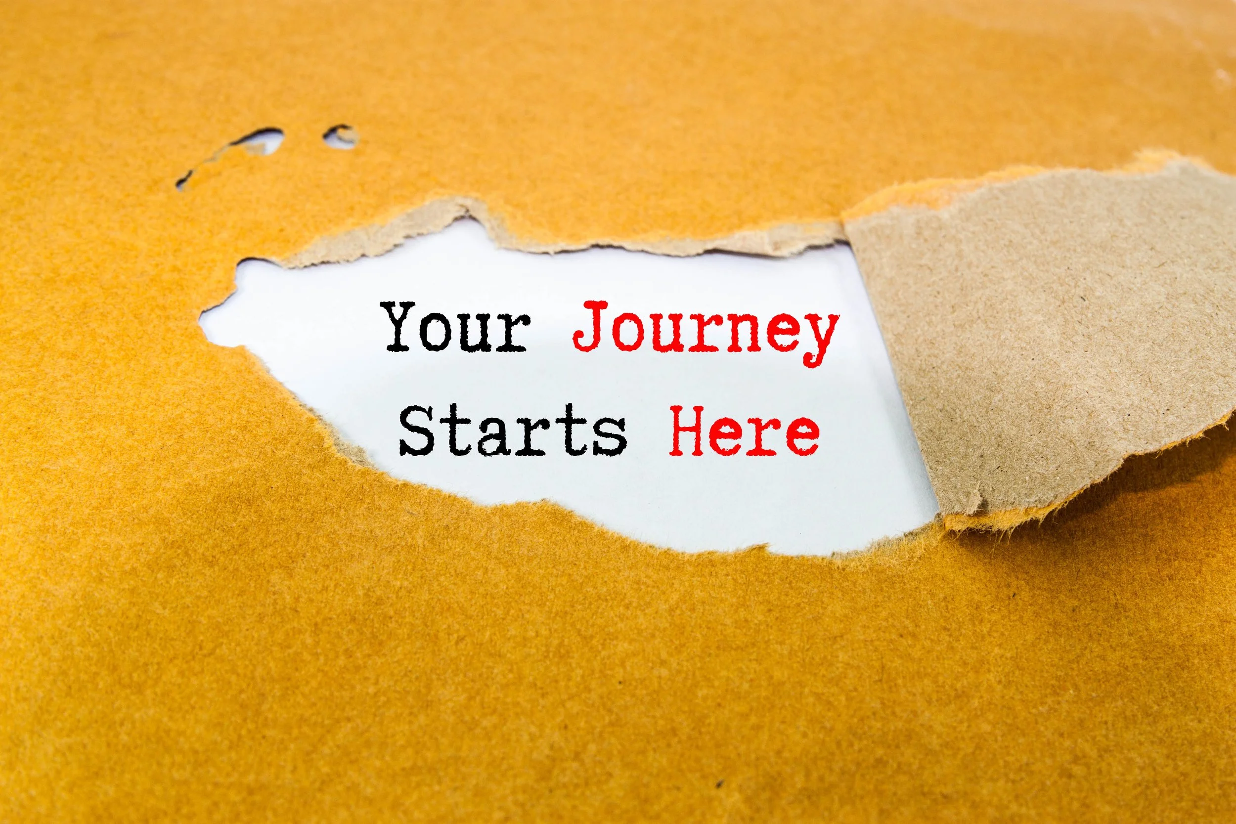 A torn piece of brown paper reveals a white background with the text 'Your Journey Starts Here' written in black and red.