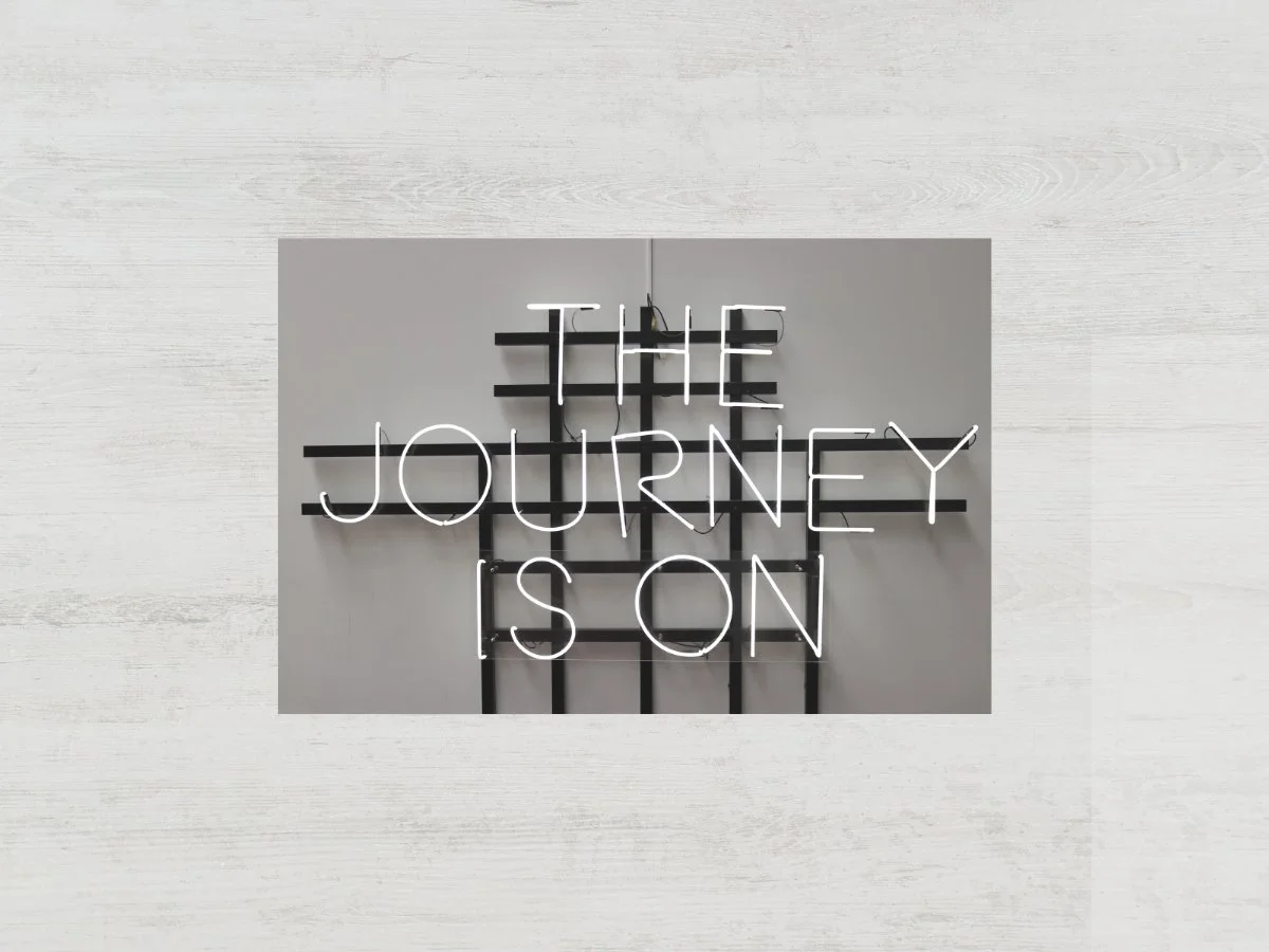 Neon sign reading 'The Journey Is On' against a gray wall.