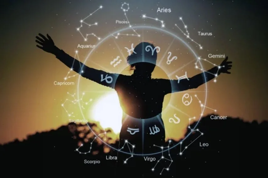A person with arms outstretched standing outdoors during sunset, with an overlay of zodiac constellations and symbols around them.