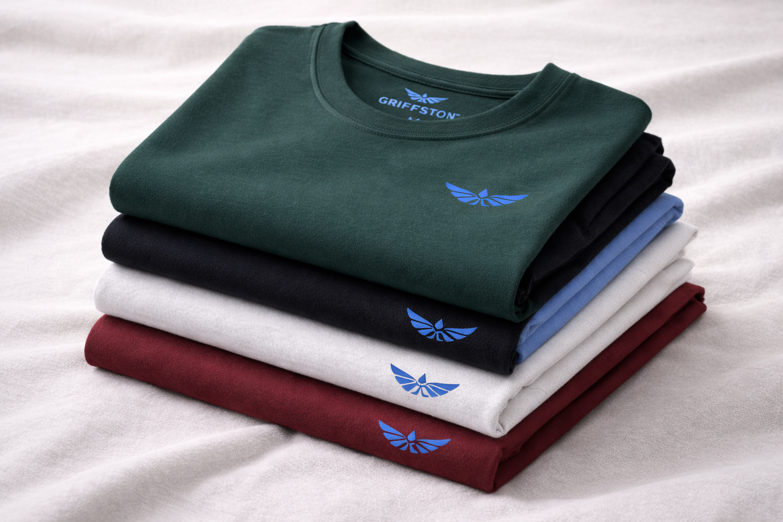 Stack of five folded T-shirts in green, black, white, blue, and red, each with a blue branded eagle logo.