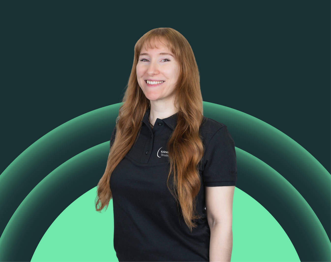 Eine lächelnde Frau mit longem, gewelltem rotbraunem Haar, trägt ein schwarzes Polo-Shirt mit einem Logo auf der Brust, vor einem geometrischen Hintergrund mit grünen und dunklen Farben.