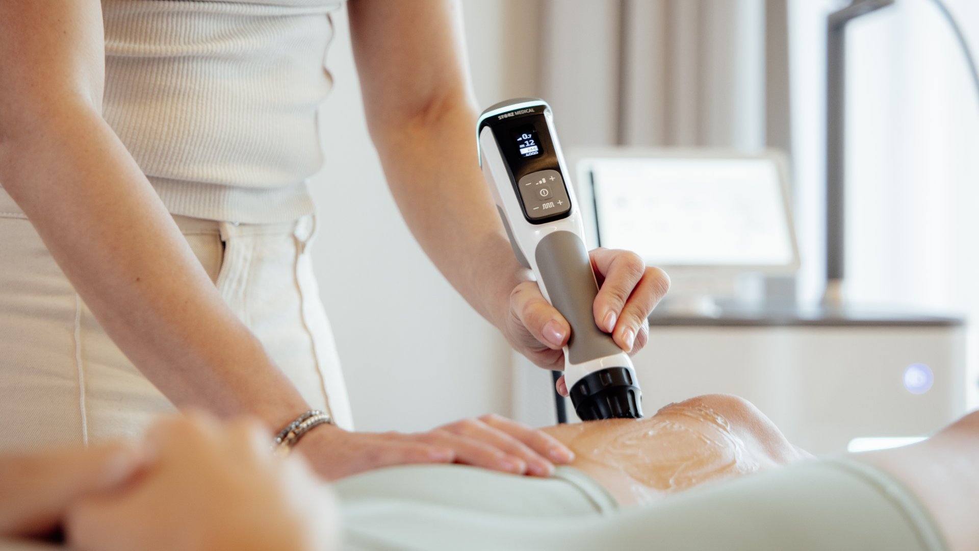 Eine Person, vermutlich eine Ärztin, führt eine Ultraschalluntersuchung am Bauch eines Patienten durch, die Ultraschallsonde wird auf den Bauch des Patienten gehalten.