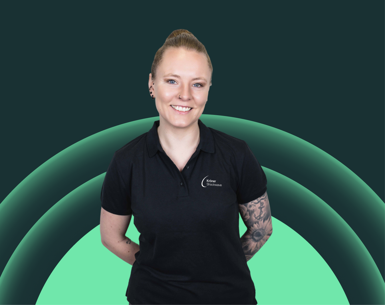 Eine Frau mit blonden Haaren in einem schwarzen Polo-Shirt, die lächelnd vor einem digital erstellten Hintergrund mit grünen konzentrischen Kreisen steht.