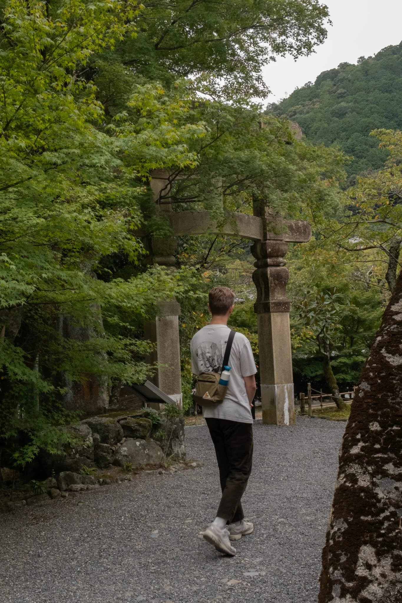 Tom van Dessel in een bosrijke omgeving met een oude stenen torii-poort.