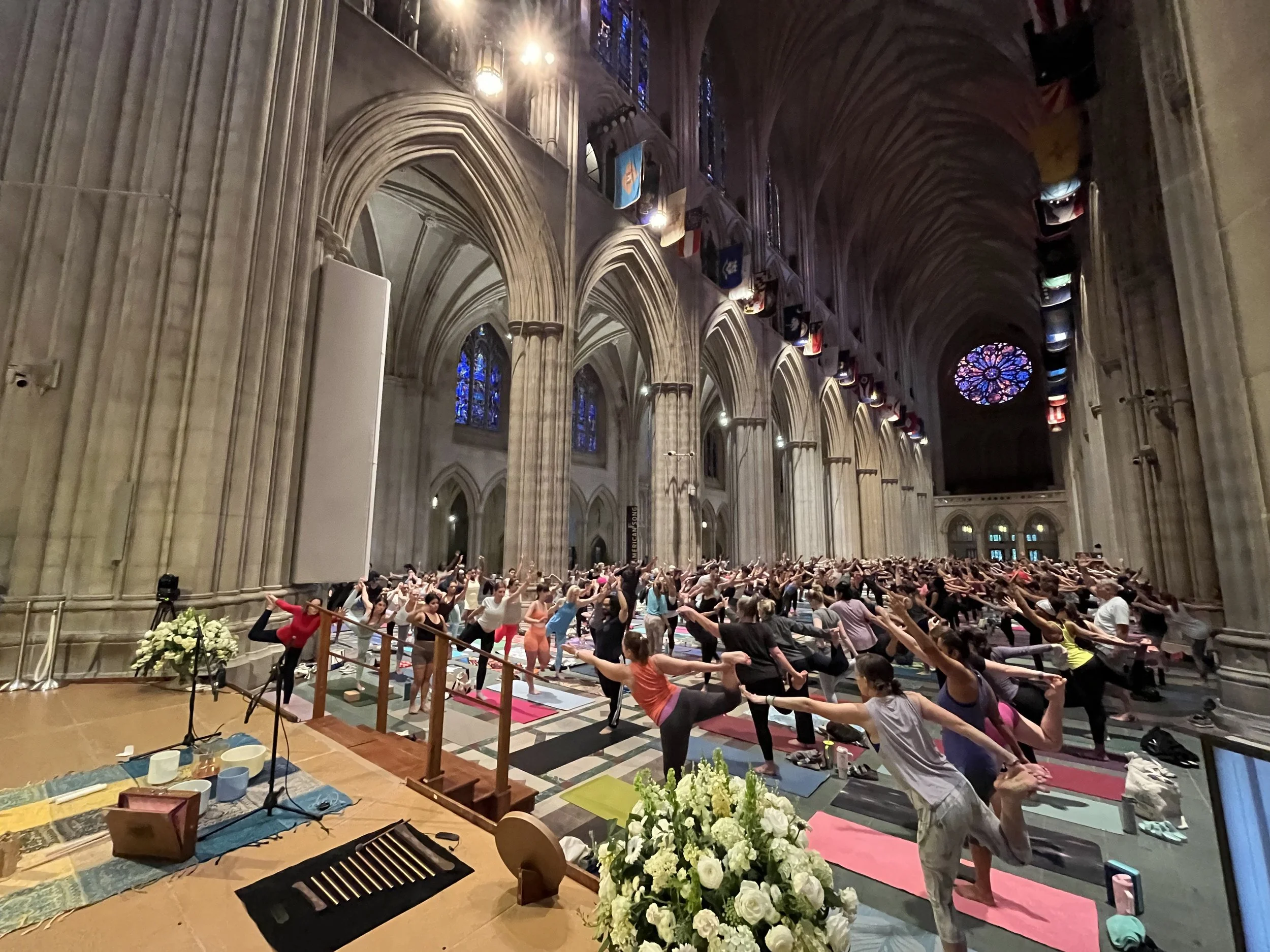 A group of 700 people in the National Cathedral participating in a yoga class and sound bath session. Participants are seated on yoga mats, following an instructor at the front.