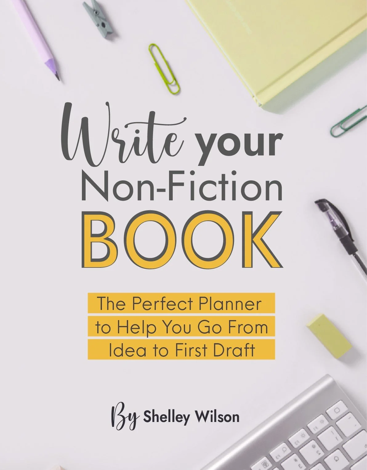 Book cover titled 'Write your Non-Fiction Book' with subtitle 'The Perfect Planner to Help You Go From Idea to First Draft' by Shelley Wilson, surrounded by office supplies like pens, paper clips, a sticky note, a notepad, and a keyboard.
