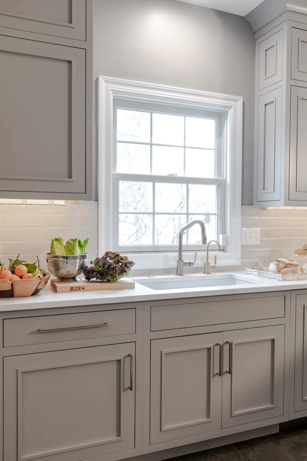 Transitional warm grey kitchen with quartz countertops, textured backsplash, professional appliances and gold fixtures.