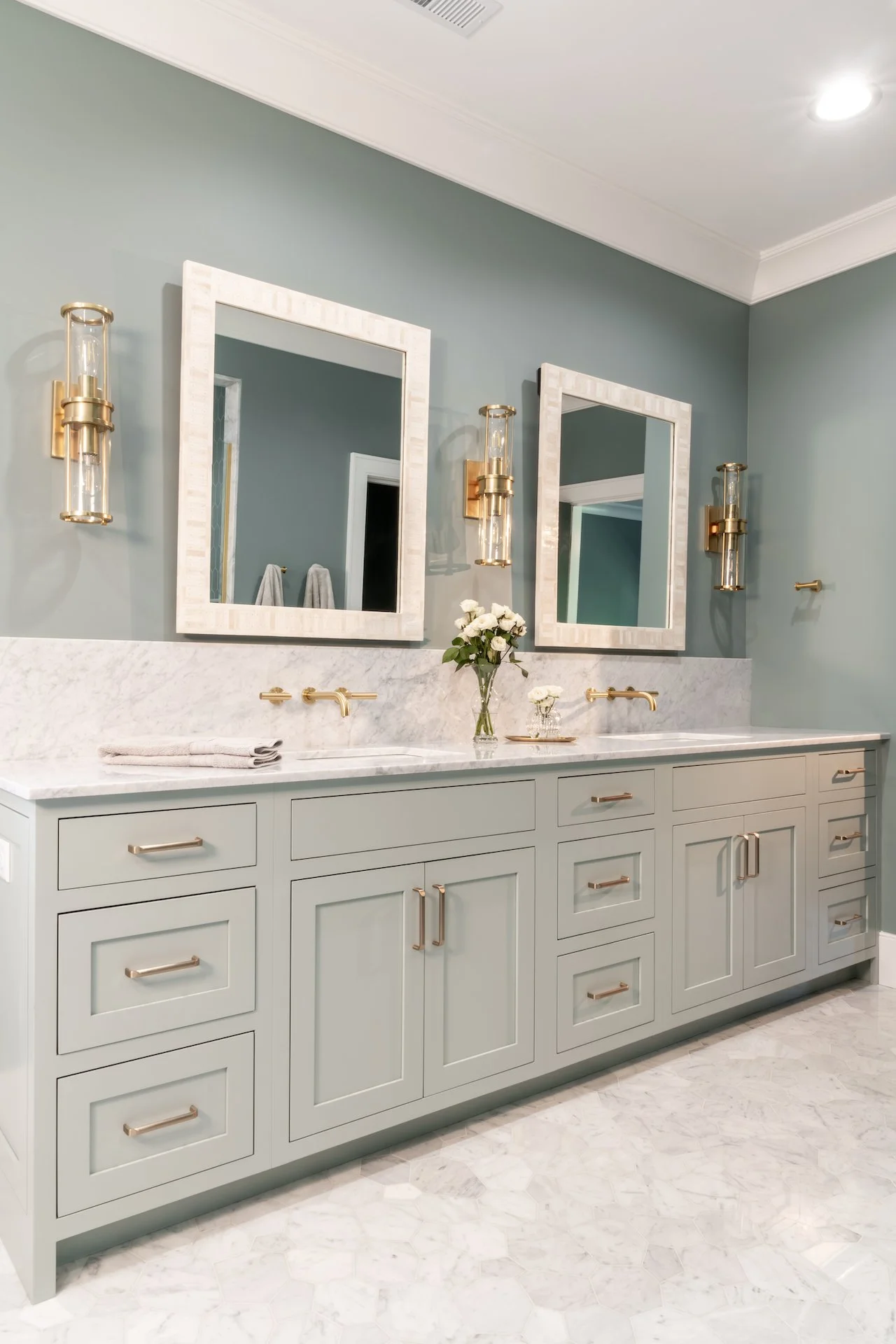 Transitional coastal blue bathroom with marble countertops and gold fixtures. 