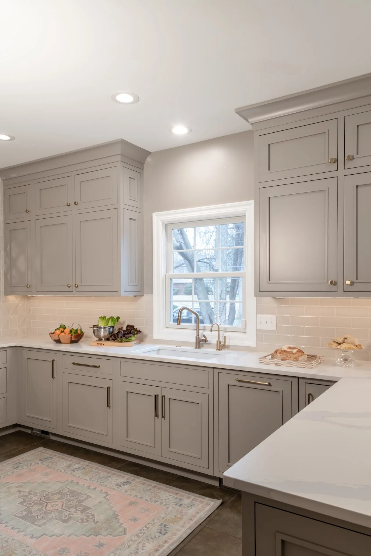 Transitional warm grey kitchen with quartz countertops, textured backsplash, professional appliances and gold fixtures.