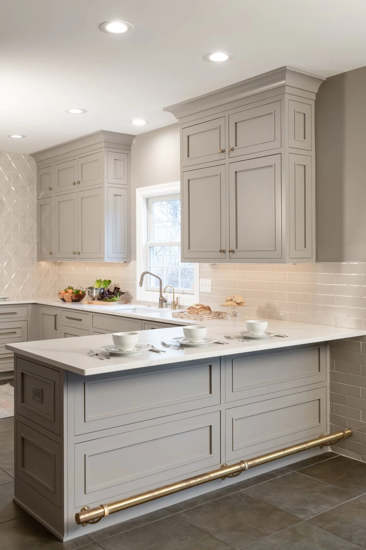 Transitional warm grey kitchen with quartz countertops, textured backsplash, professional appliances and gold fixtures.