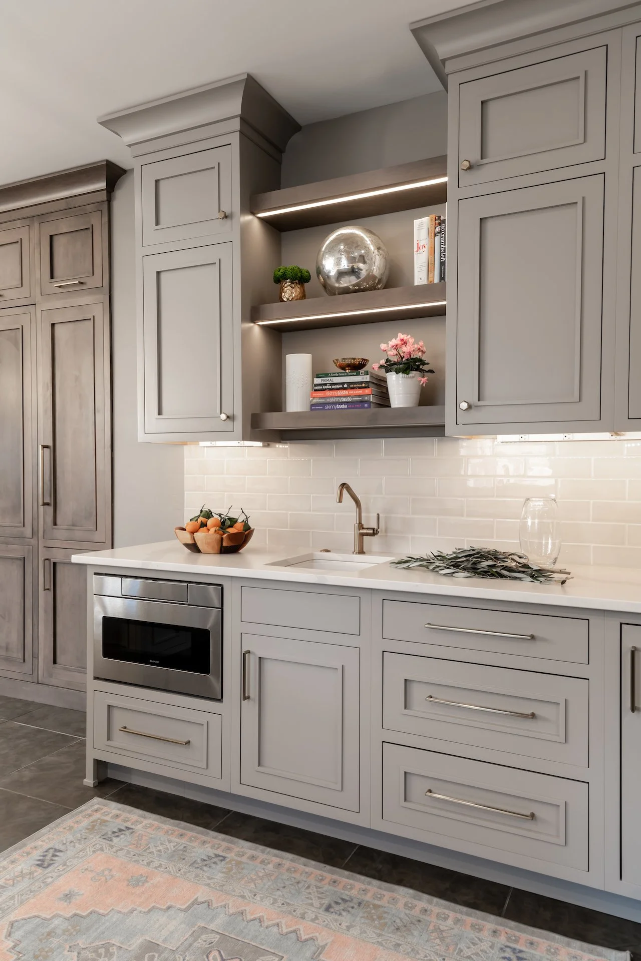 Transitional warm grey kitchen with quartz countertops, textured backsplash, professional appliances and gold fixtures.