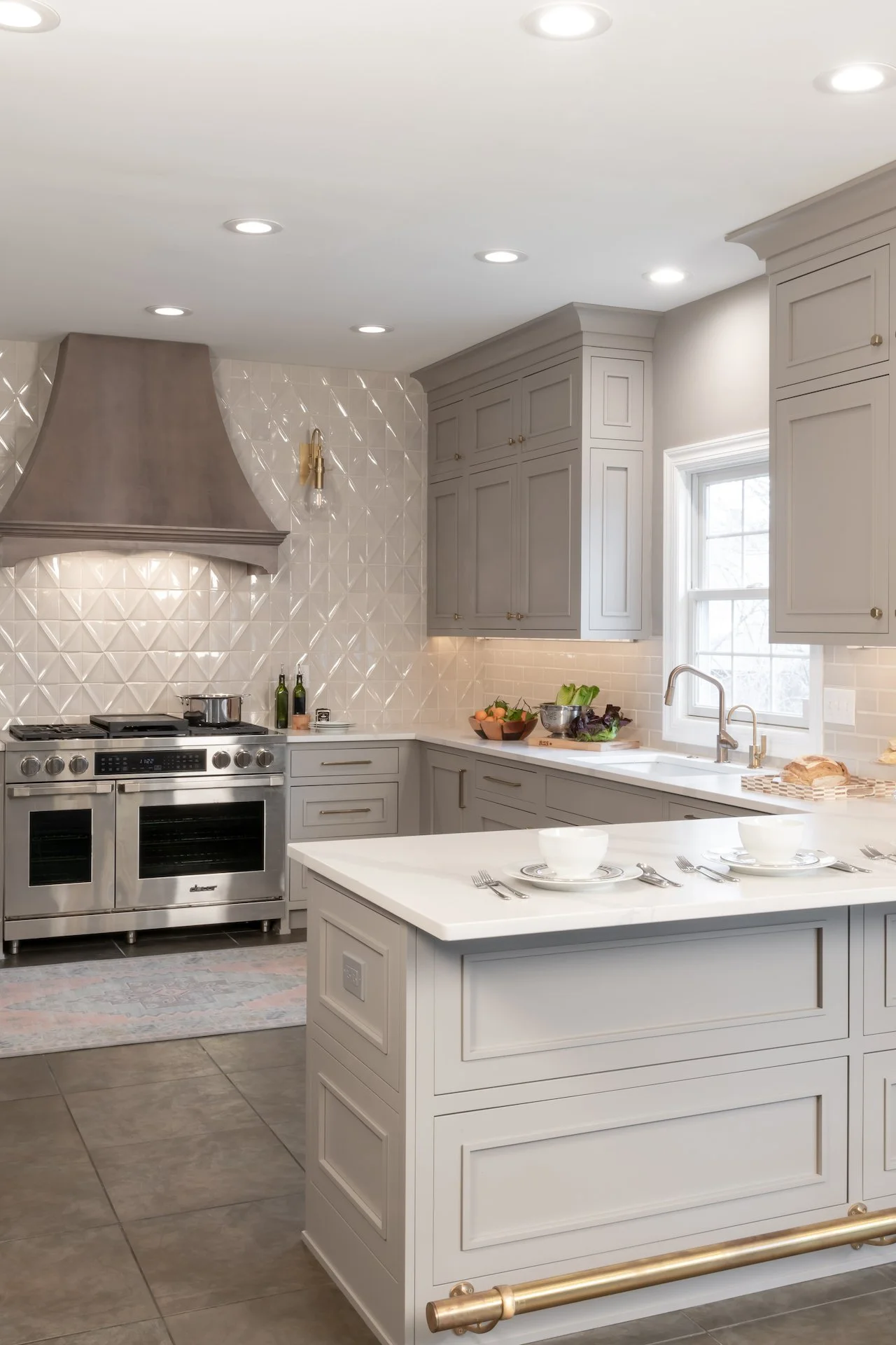 Transitional warm grey kitchen with quartz countertops, textured backsplash, professional appliances and gold fixtures.