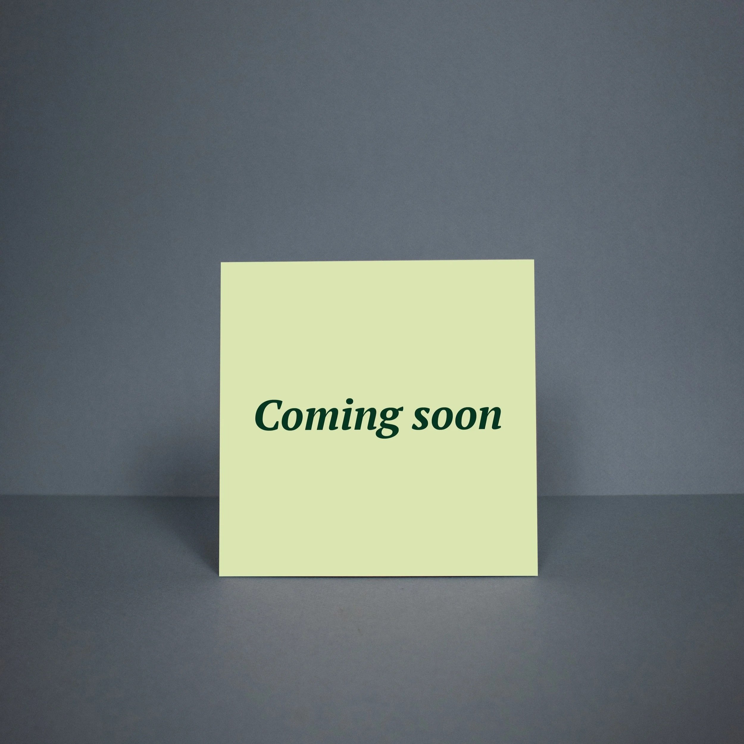 Een licht groen bord met de tekst 'Coming soon', geplaatst op een donker blauwe/grijze achtergrond.