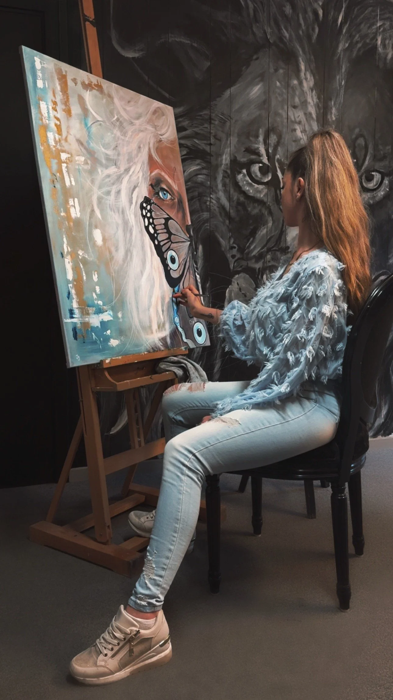 En kvinde maler et kunstværk med en sommerfugl på lærredet i et kunststue.