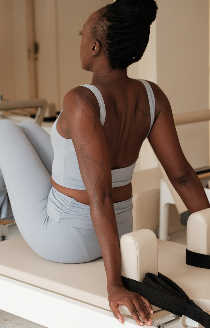 Une femme assise sur une table d'hôpital vue de dos, portant une tenue de sport gris clair, avec des tatouages sur le bras, dans un environnement médical.