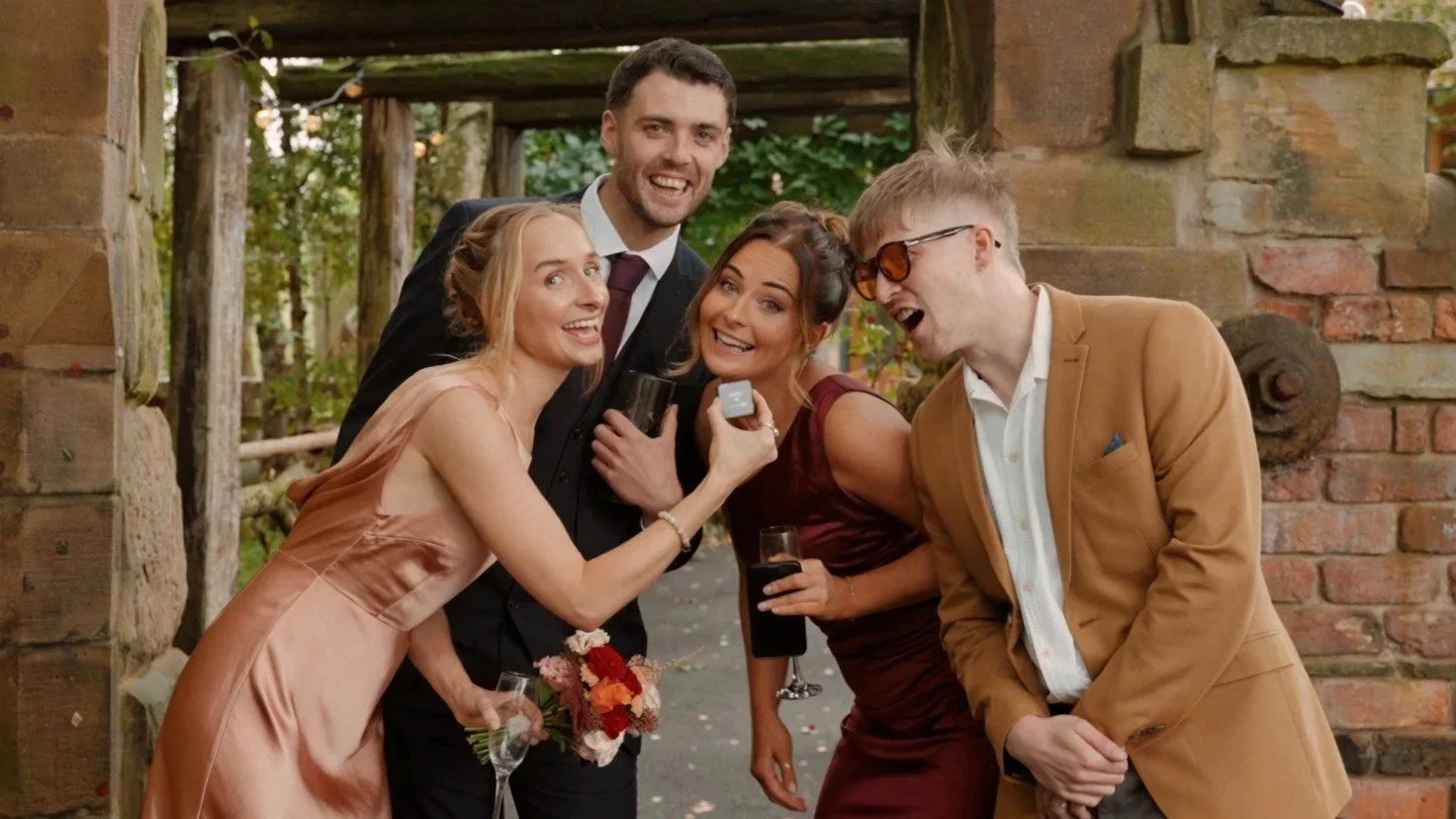 Group of friends dressed up and smiling at a wedding, speaking to camera to leave a message in the couple’s video guestbook.