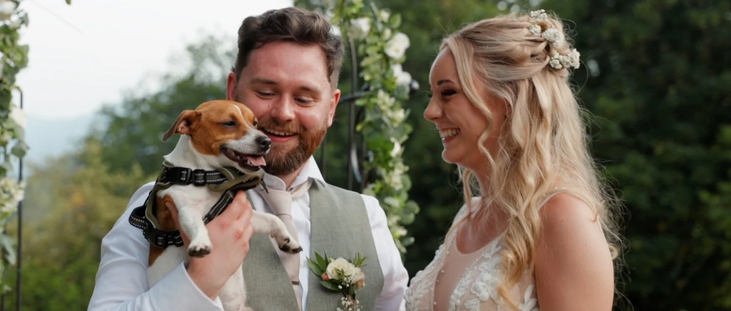 A bride and groom smiling at each other with a dog while dancing at their wedding at the Merewood Country House Hotel in Windermere, Lake District.