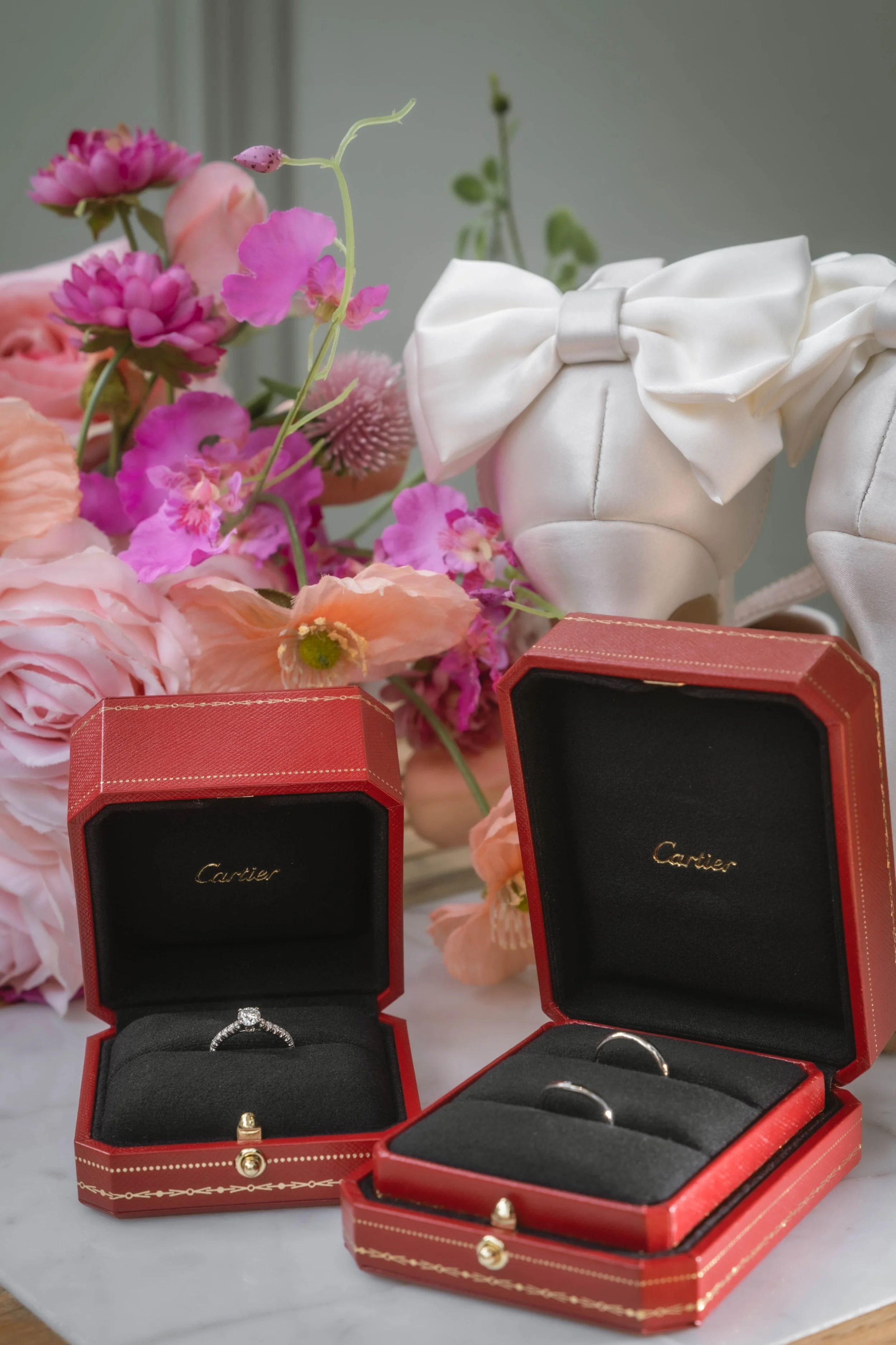 カルティエのリングが入った赤い宝石箱が二つと、ピンクと白の花と白いリボンの装飾が飾られている