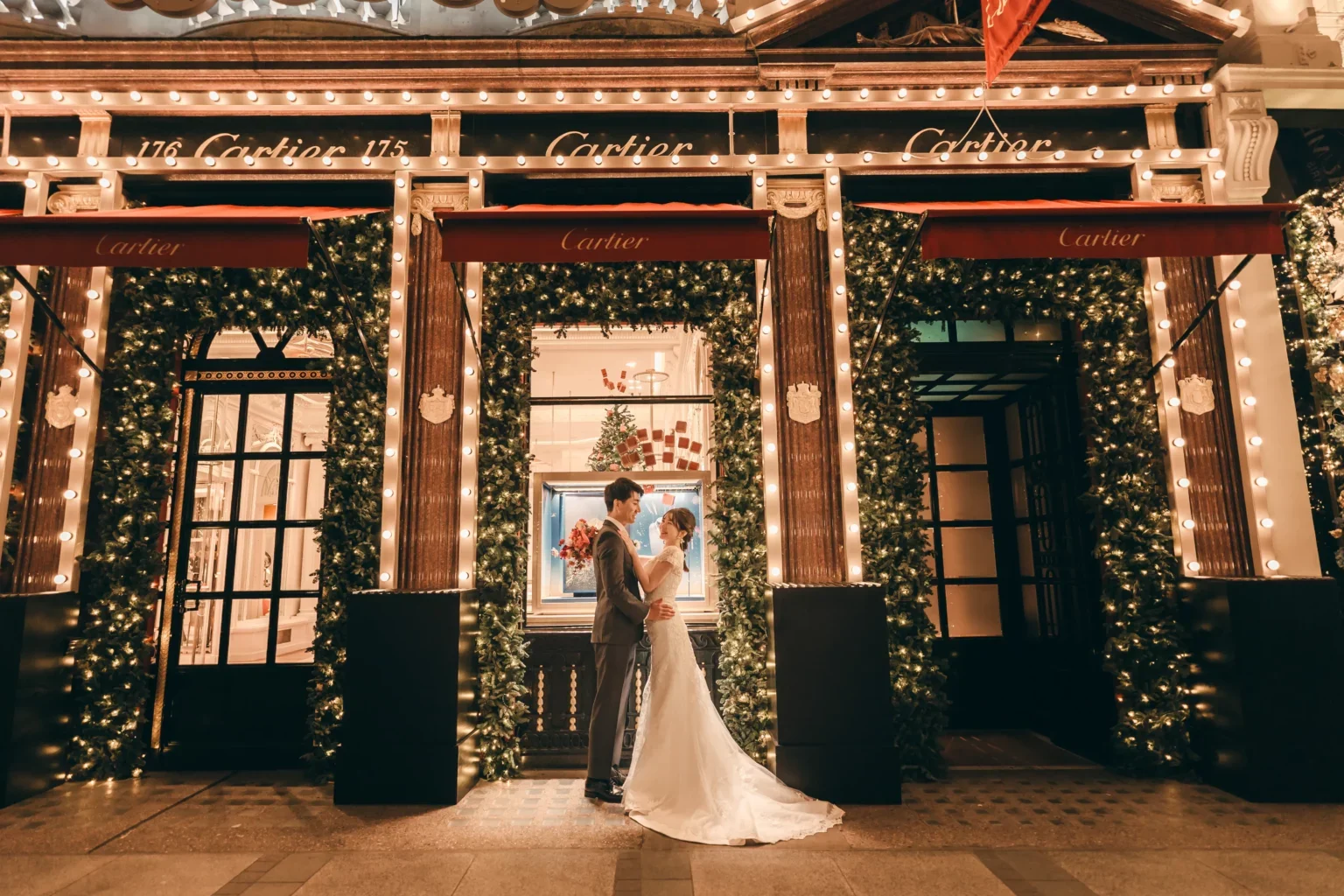 クリスマスマーケットのような装飾の中で、結婚祝いのカップルが抱き合っているシーン。背景にはクリスマスツリーと飾り付けが見える。