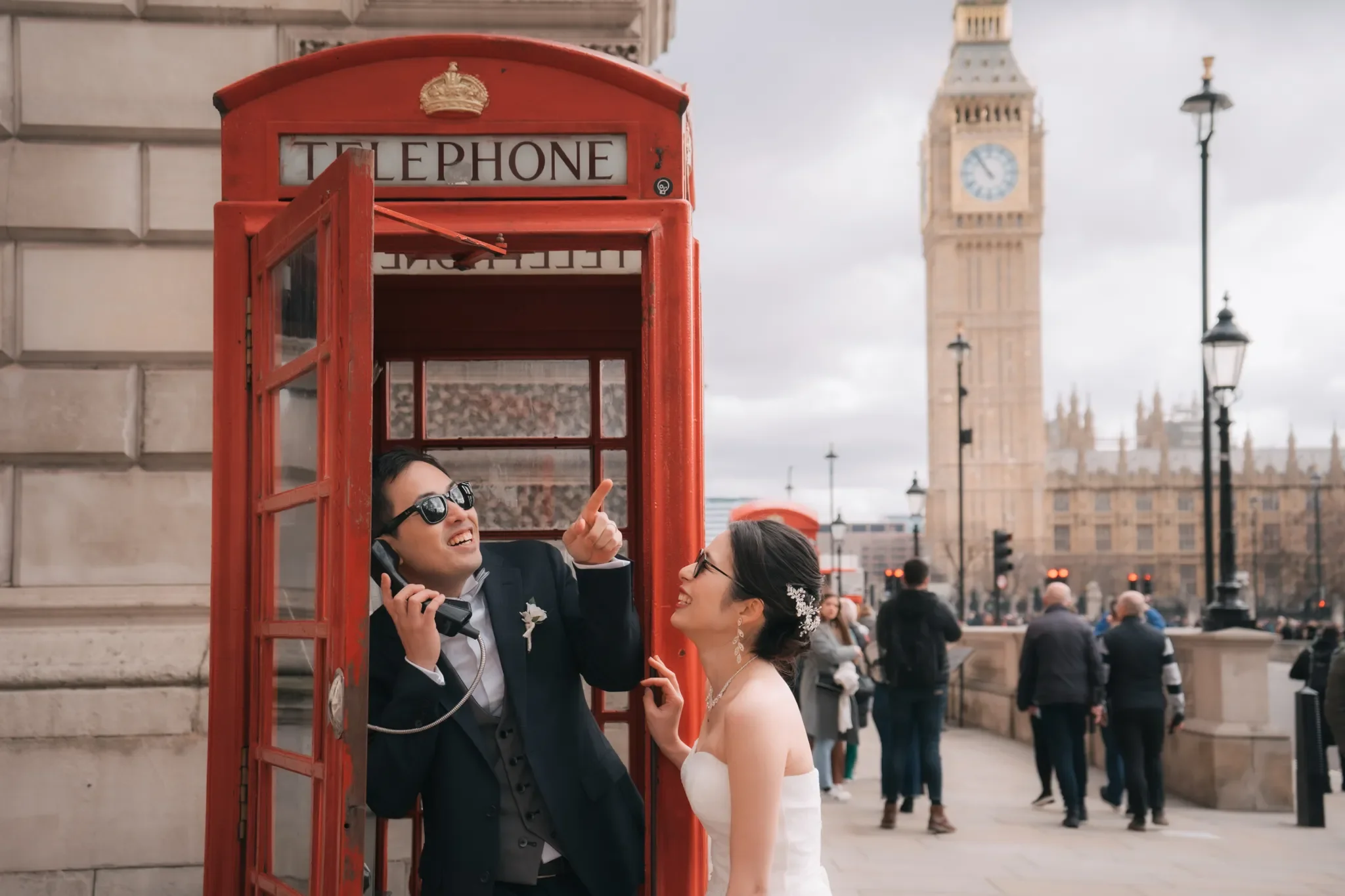結婚式を挙げたカップルが赤い電話ボックスの前で楽しそうに話している。背景にはロンドンのビッグ・ベンとイギリスの街並みが見える。