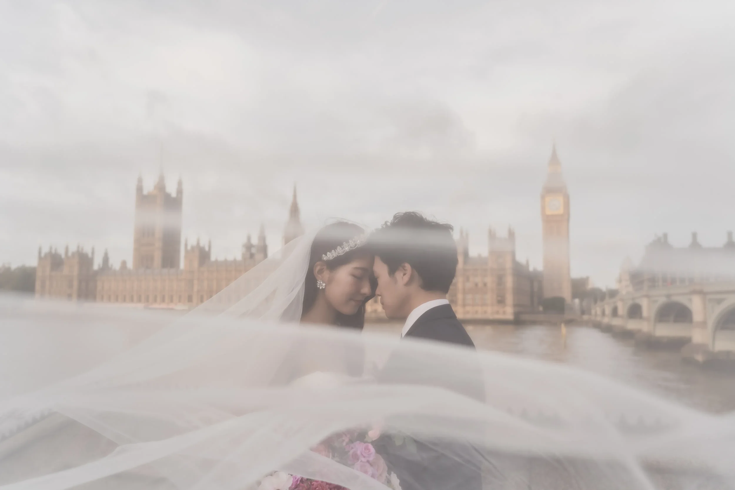 イギリスのビッグベンと国会議事堂を背景に、結婚式を挙げた新郎新婦が顔を寄せ合っている写真。