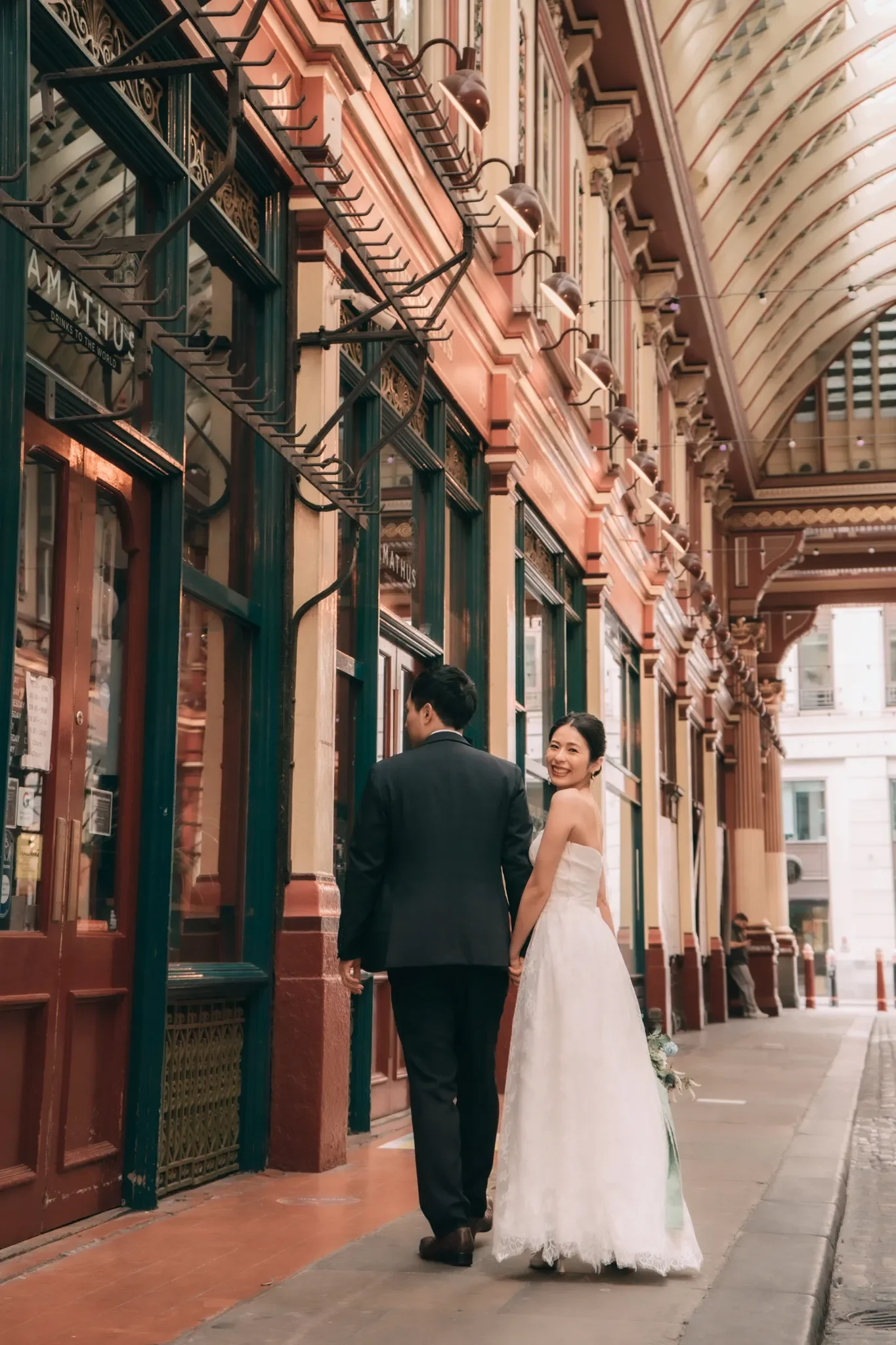 結婚式の花嫁と花婿が街のレトロなアーケードの中で手を繋ぎながら振り向いて笑っている写真
