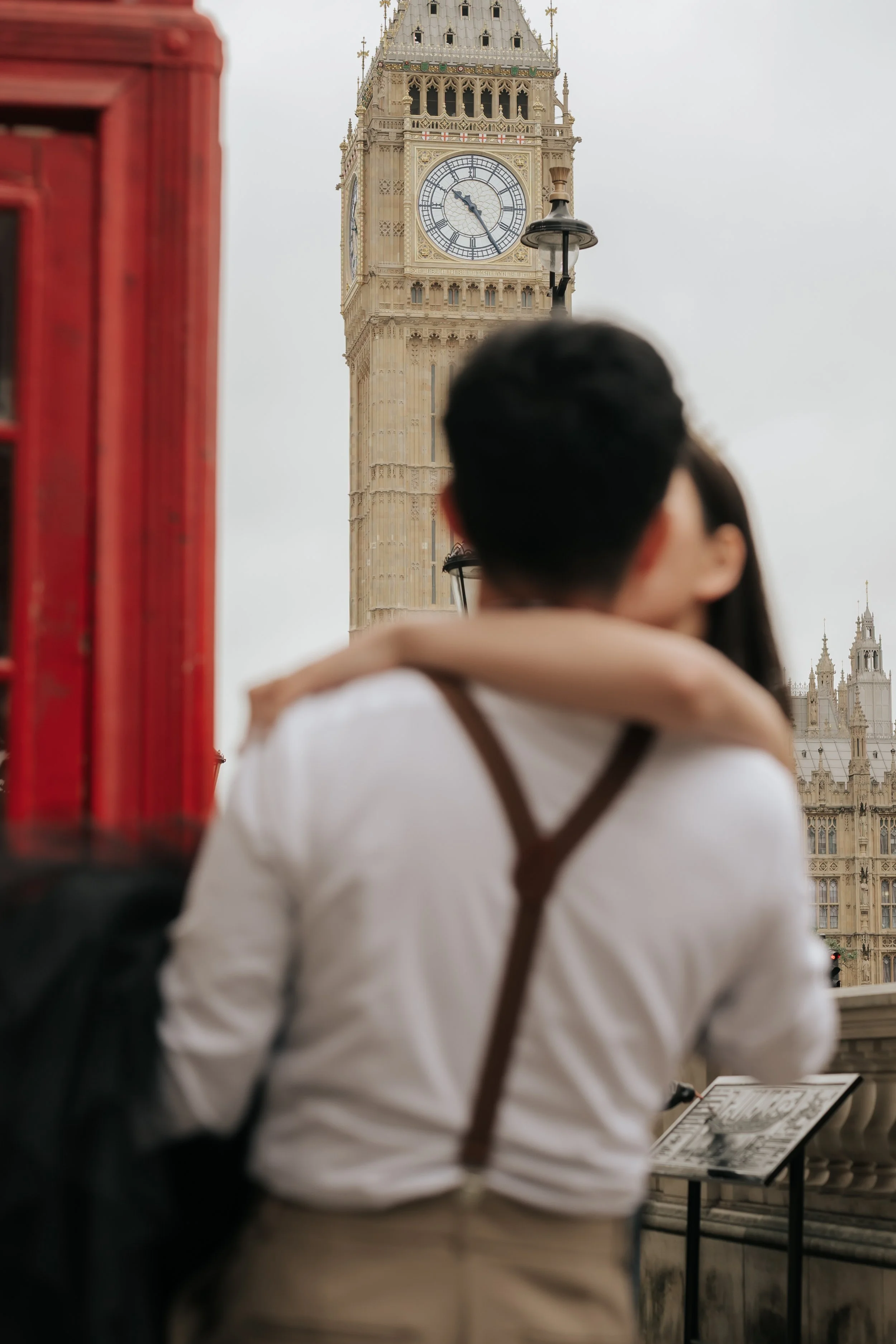 ロンドンのウェストミンスター橋の上でカップルが抱き合っている。背景にビッグ Ben 時計塔が見える。