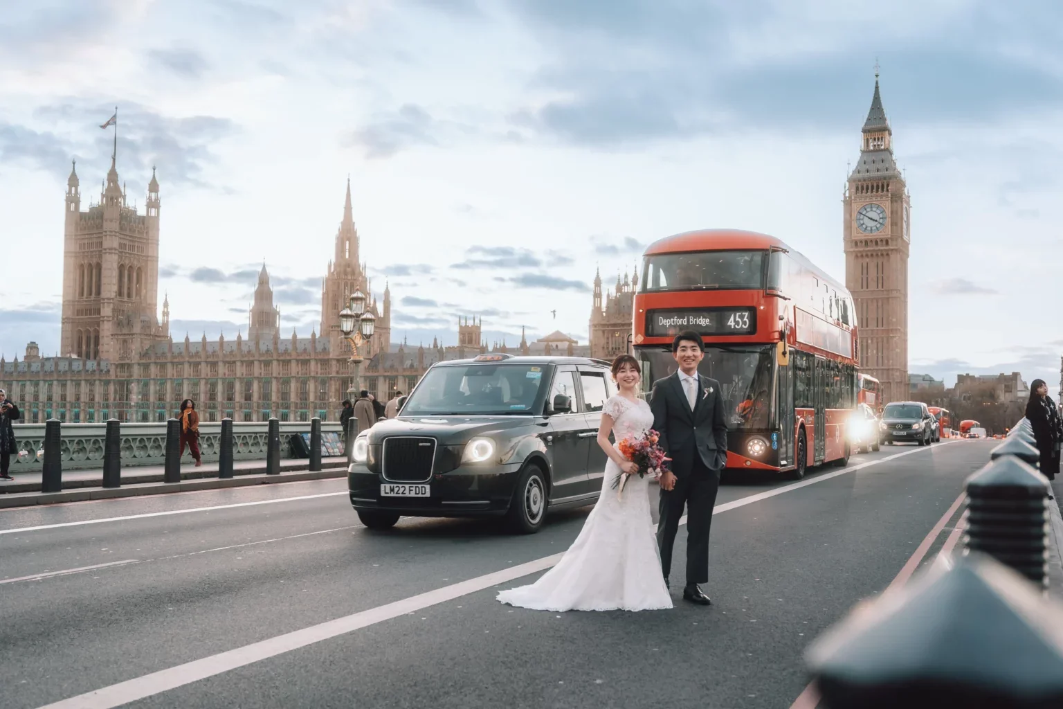 ロンドンの橋の上で、結婚したカップルが写真を撮っている。背景にビッグベンと議会議事堂が見える、夕方の風景です。