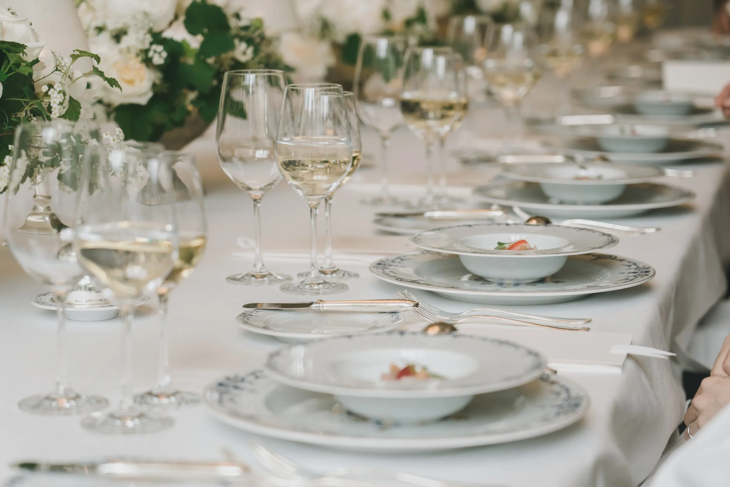 白いテーブルにワイングラスと食器が並べられ、花の飾り付けが施されているエレガントな食事のセッティング