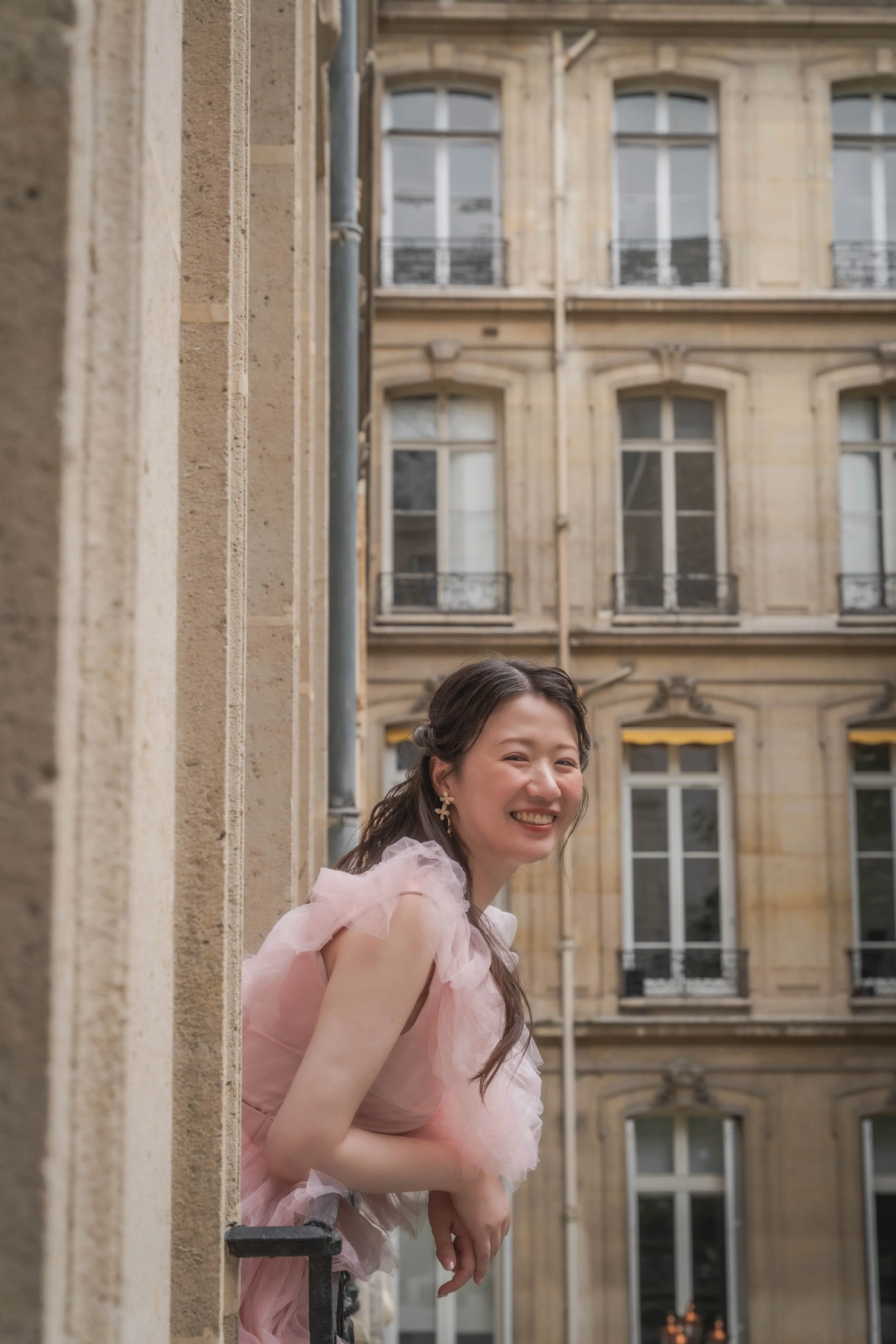 ピンクのドレスを着た女性が笑顔でバルコニーから外を見ている