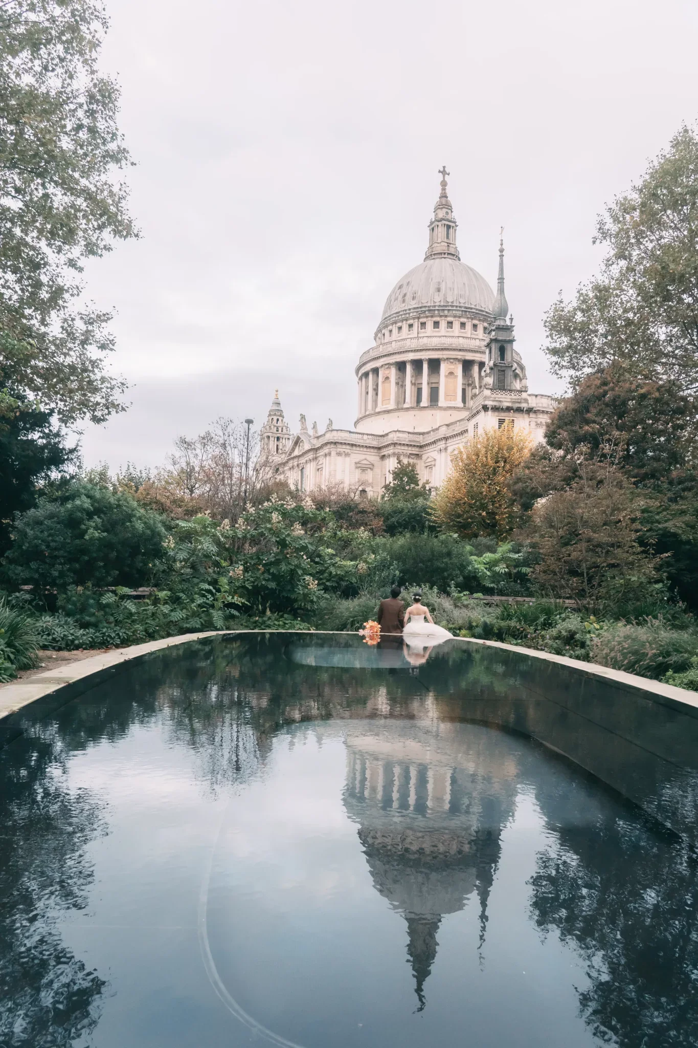 ロンドンのセント・ポール大聖堂を背景にした結婚するカップルが池のそばに座っている風景