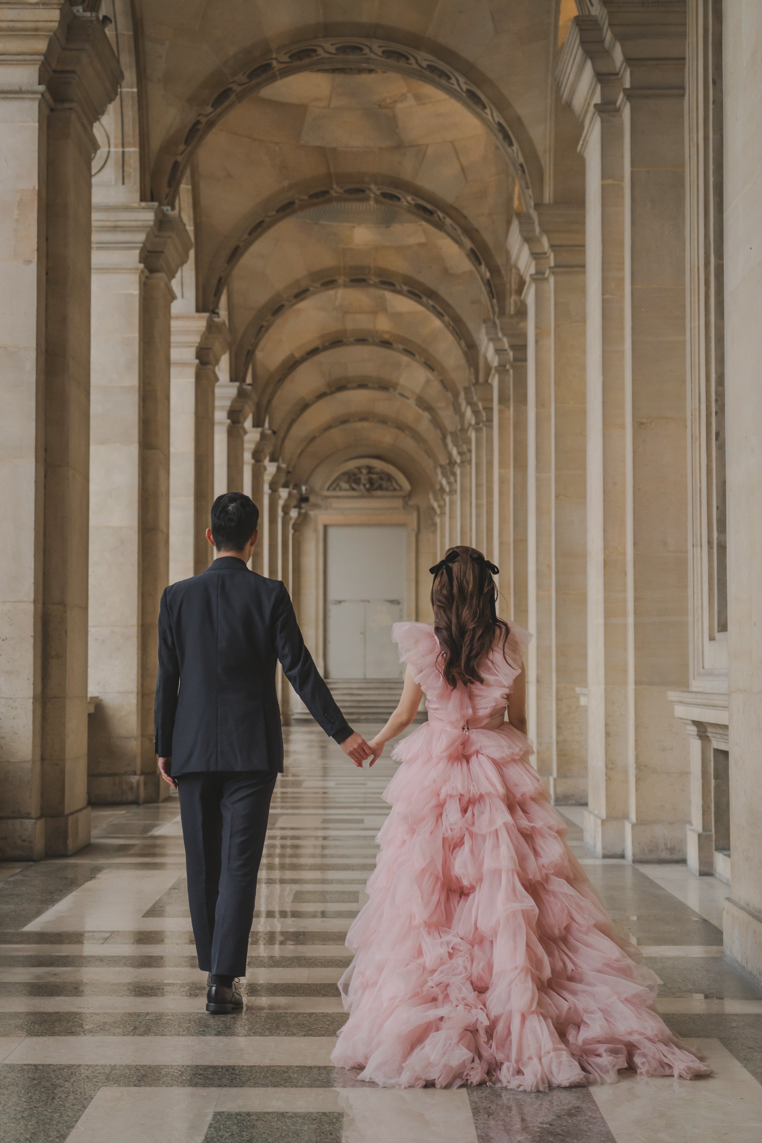 結婚式のドレスを着た女性とスーツ姿の男性が手をつないで廊下を歩いている。