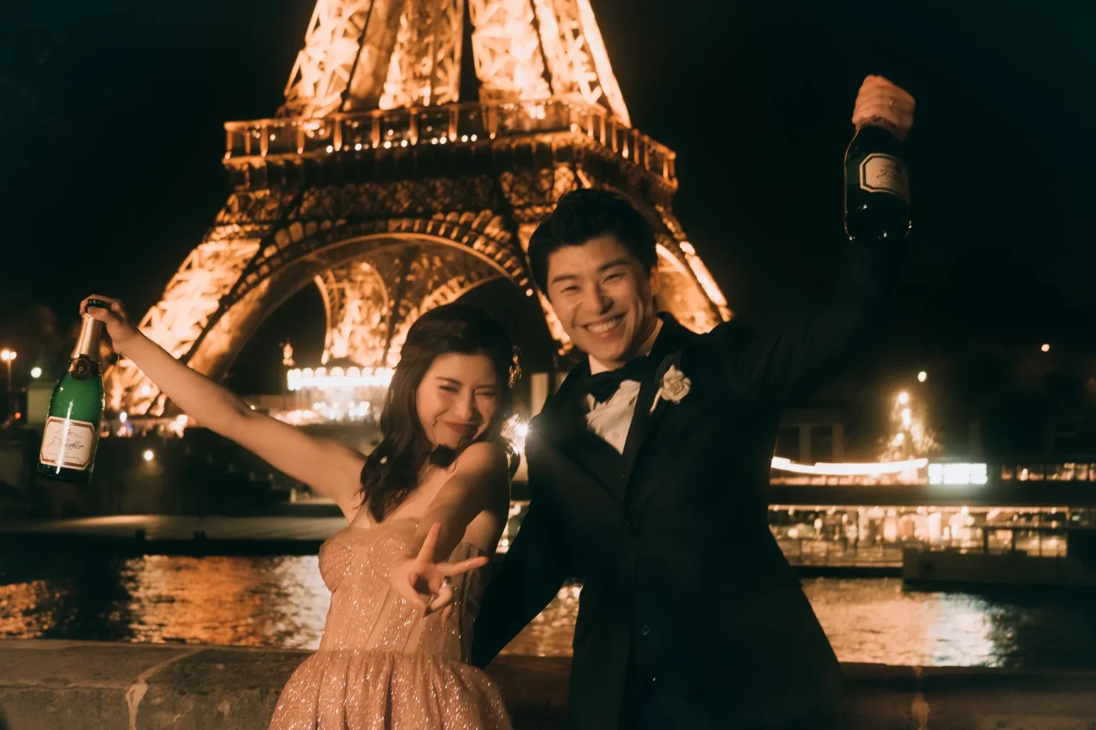 エッフェル塔の前で祝うカップル、夜にシャンパンを持ち笑顔でポーズ